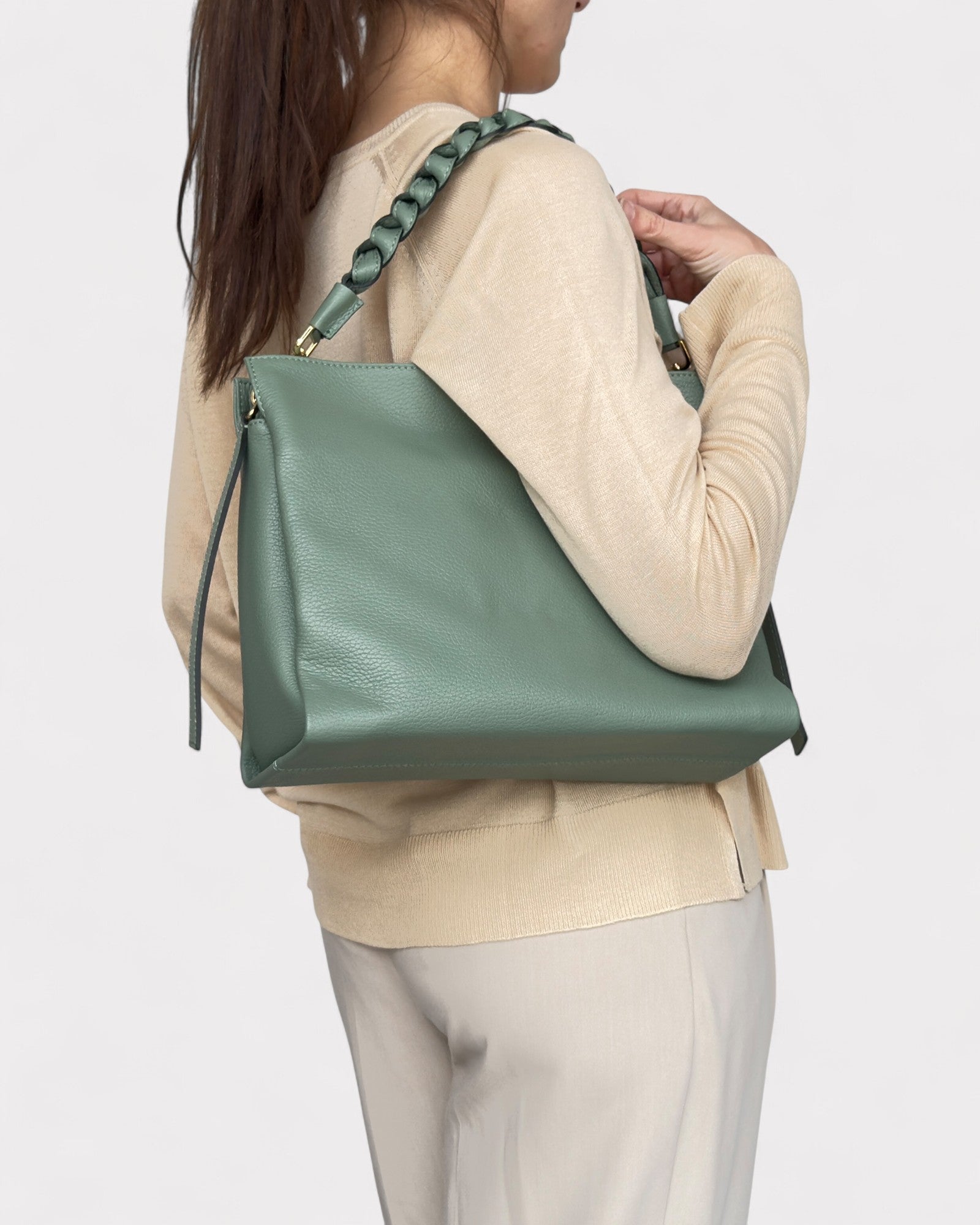 Person wearing a light beige sweater and holding a sage handbag on a white background