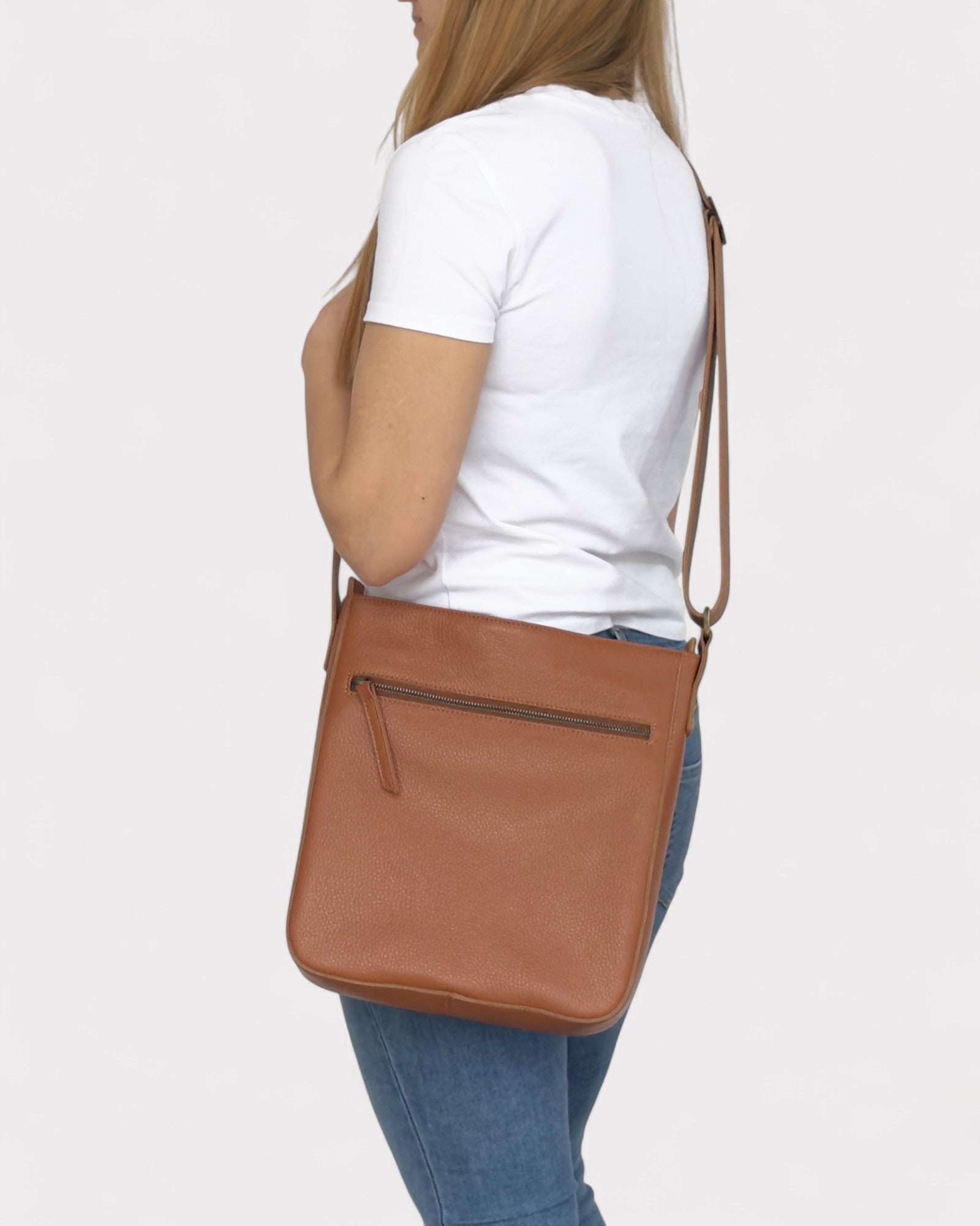 Person wearing a tan crossbody bag on a white background