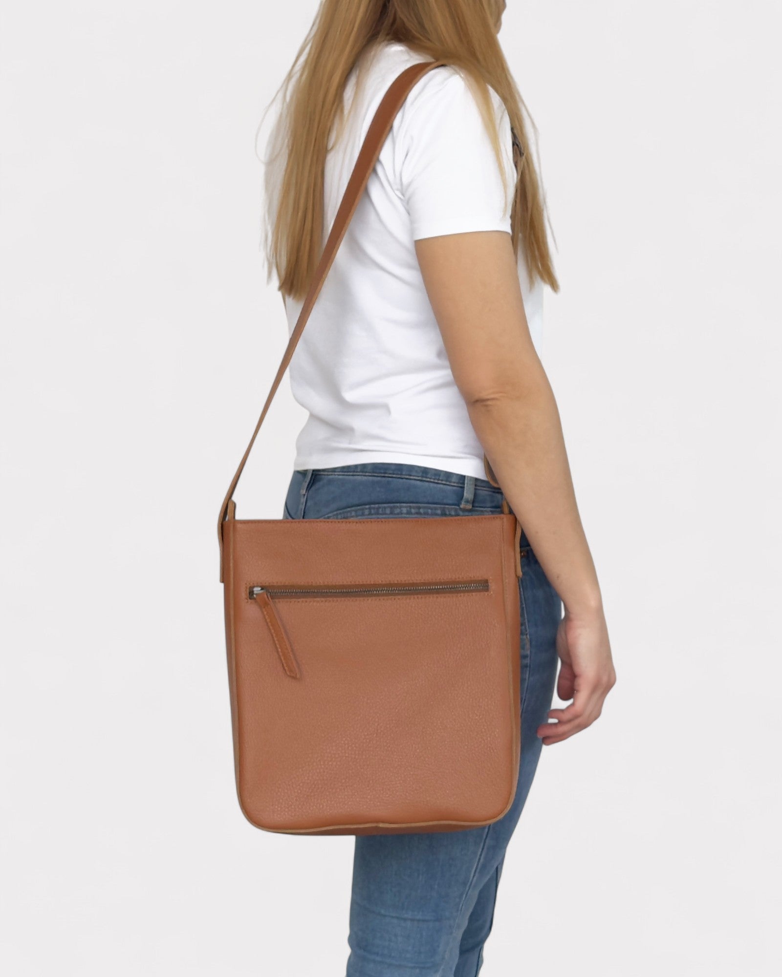 Person wearing a tan crossbody bag on a white background