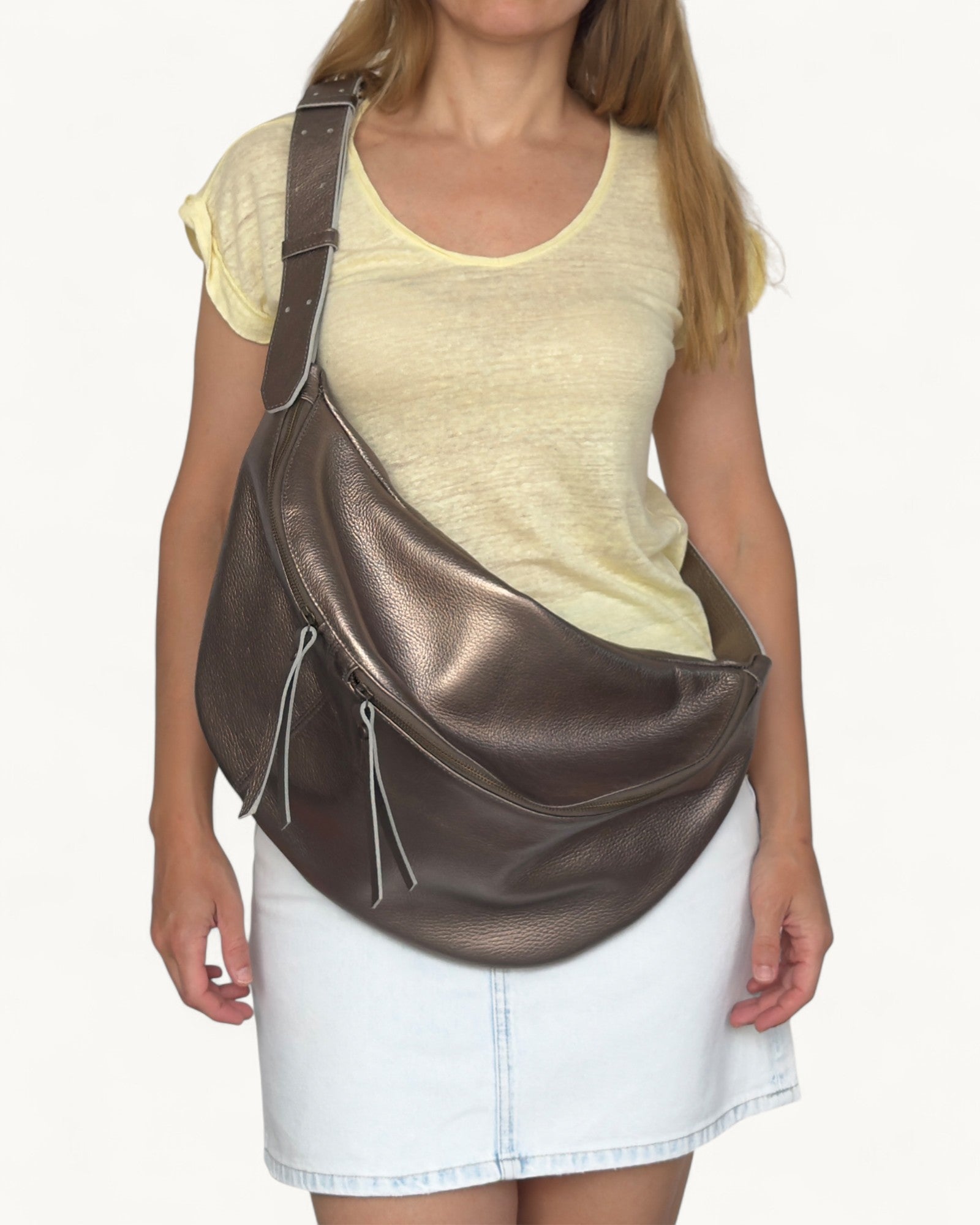 Woman carrying a metallic bronze leather sling bag on a white background
