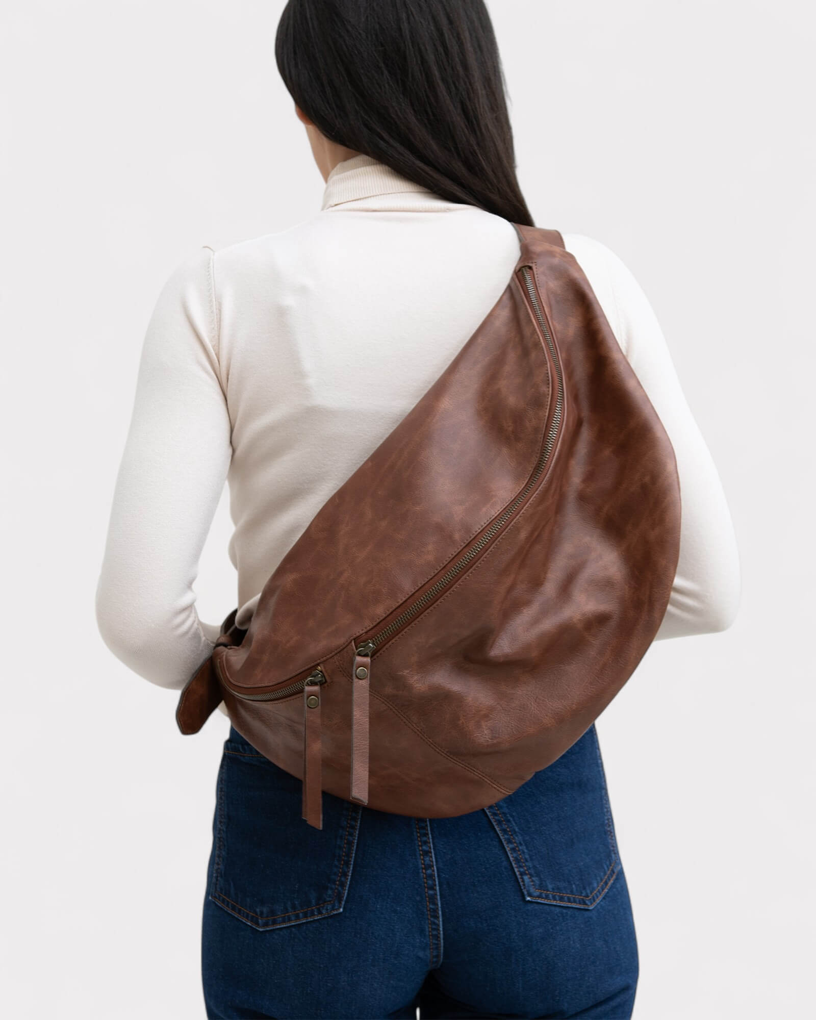 Person wearing a brown leather sling bag on a plain background