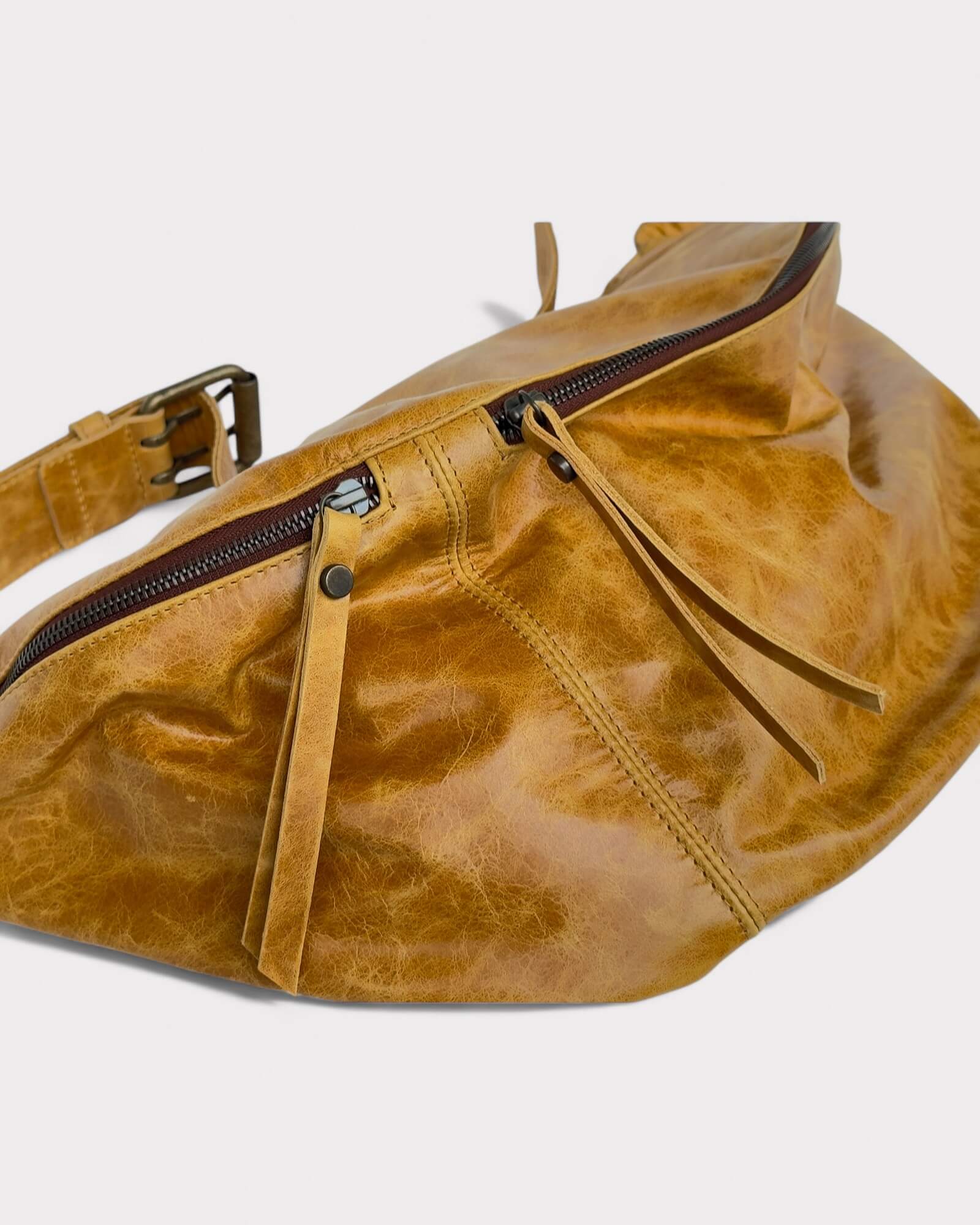 Tan leather waist bag with a zipper on a light gray background
