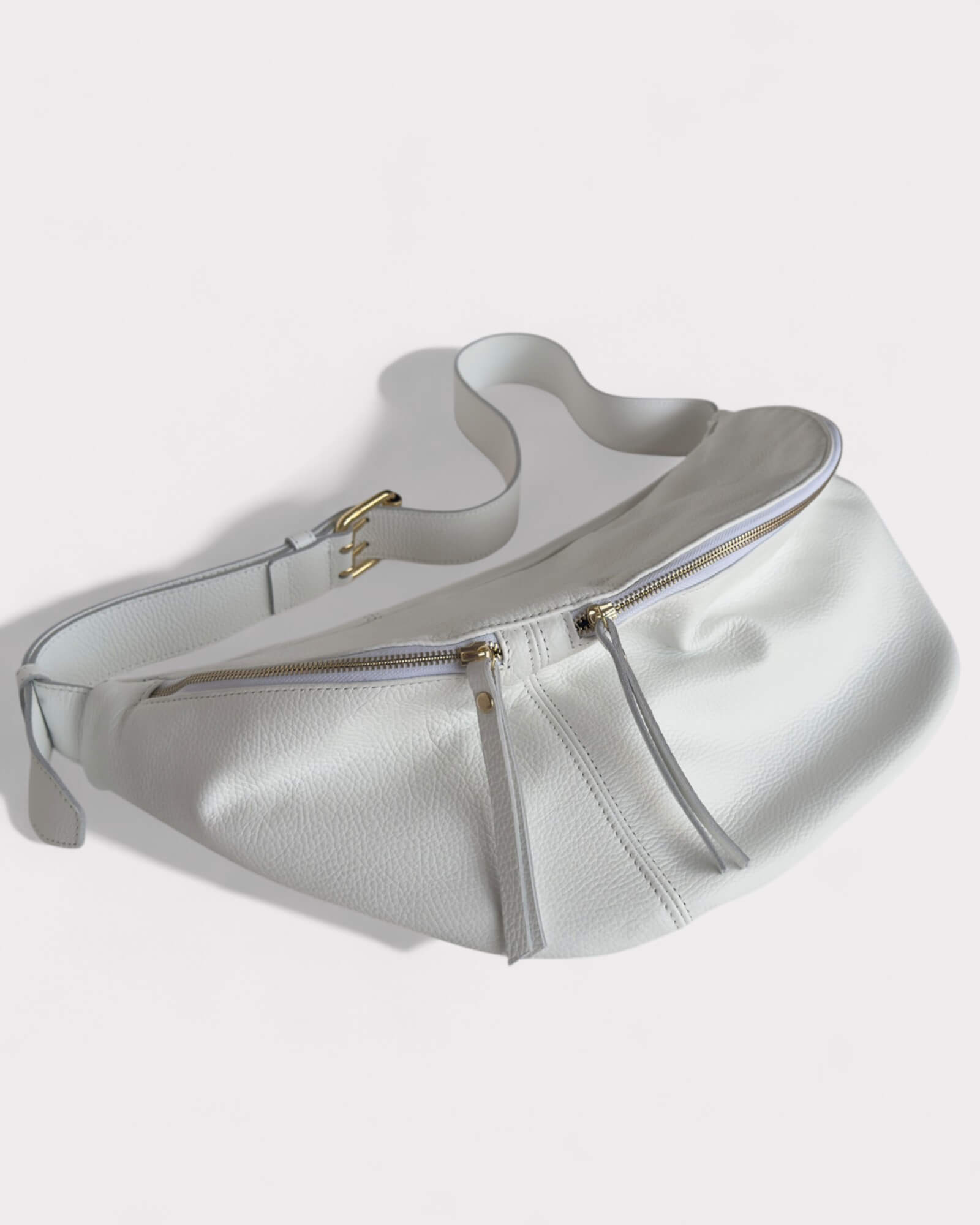 White sling bag with a gold zipper on a light gray background