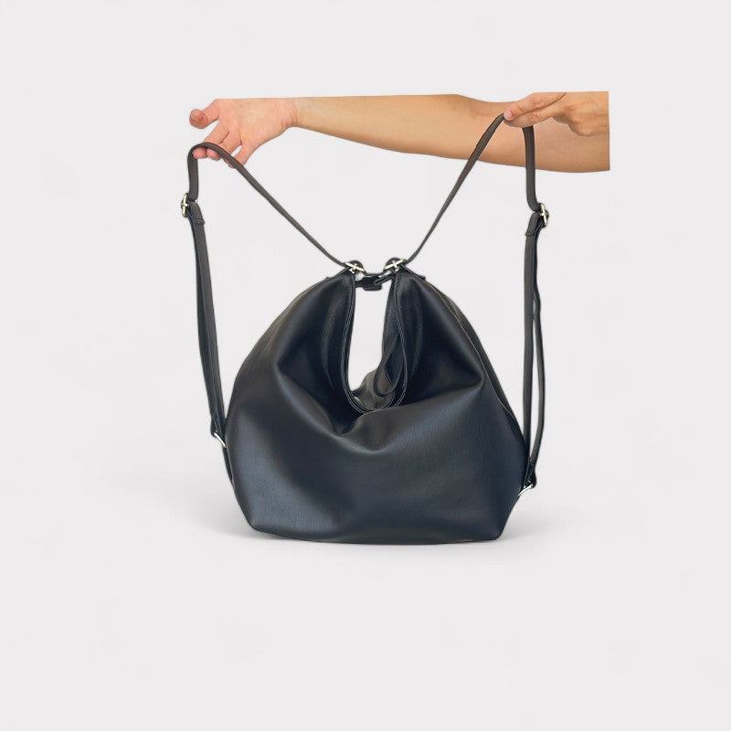 Black leather handbag held by a person against a light gray background