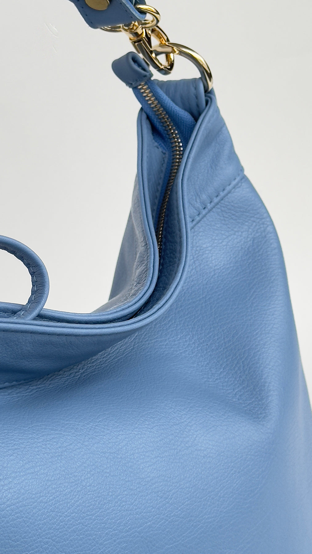 Close-up of a blue handbag with a gold zipper on a light gray background