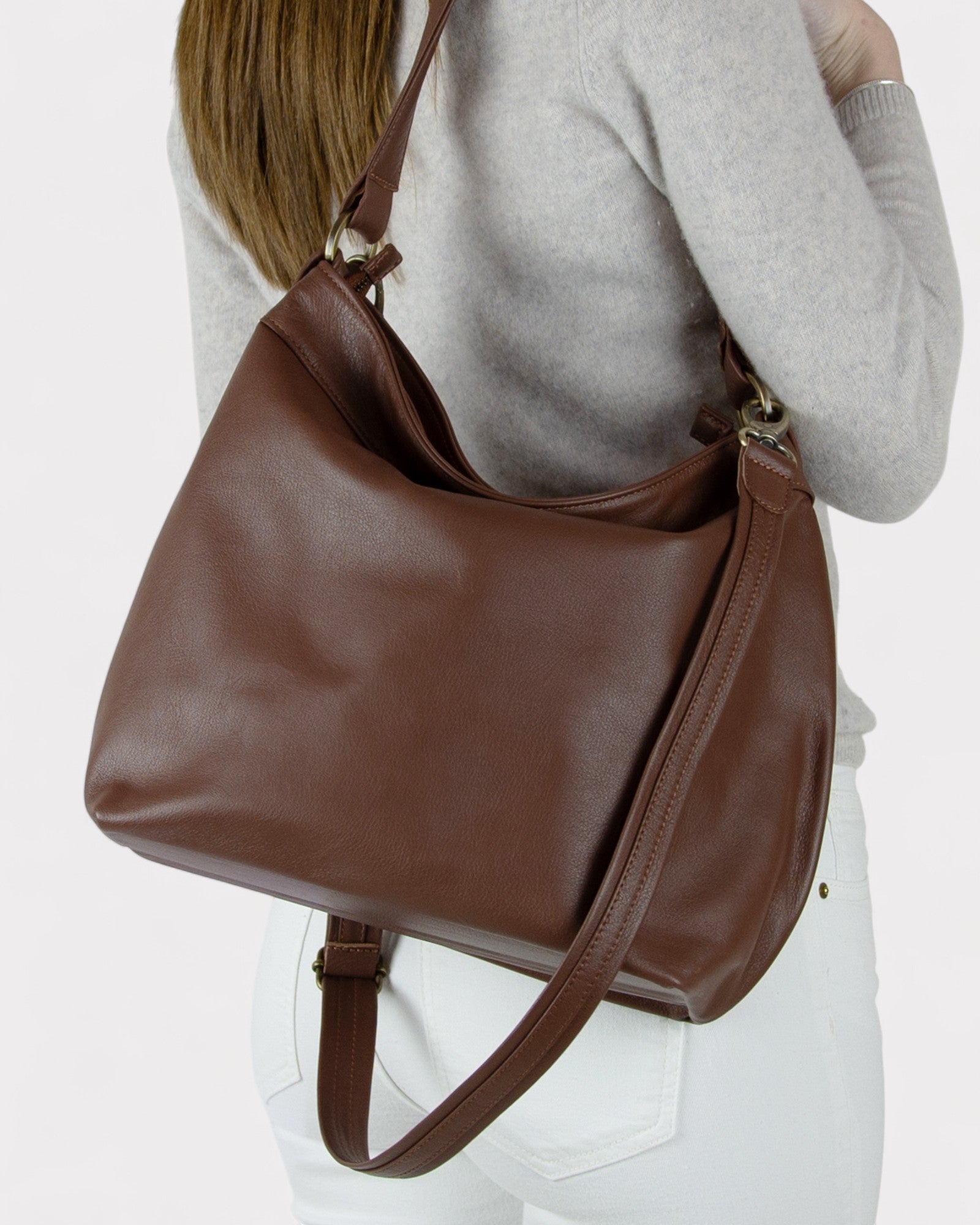 Brown leather handbag worn by a person on a white background