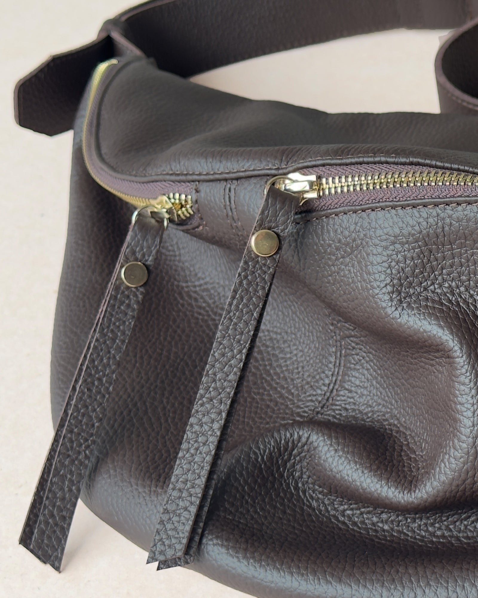 Brown leather fanny pack with gold zipper on a light background