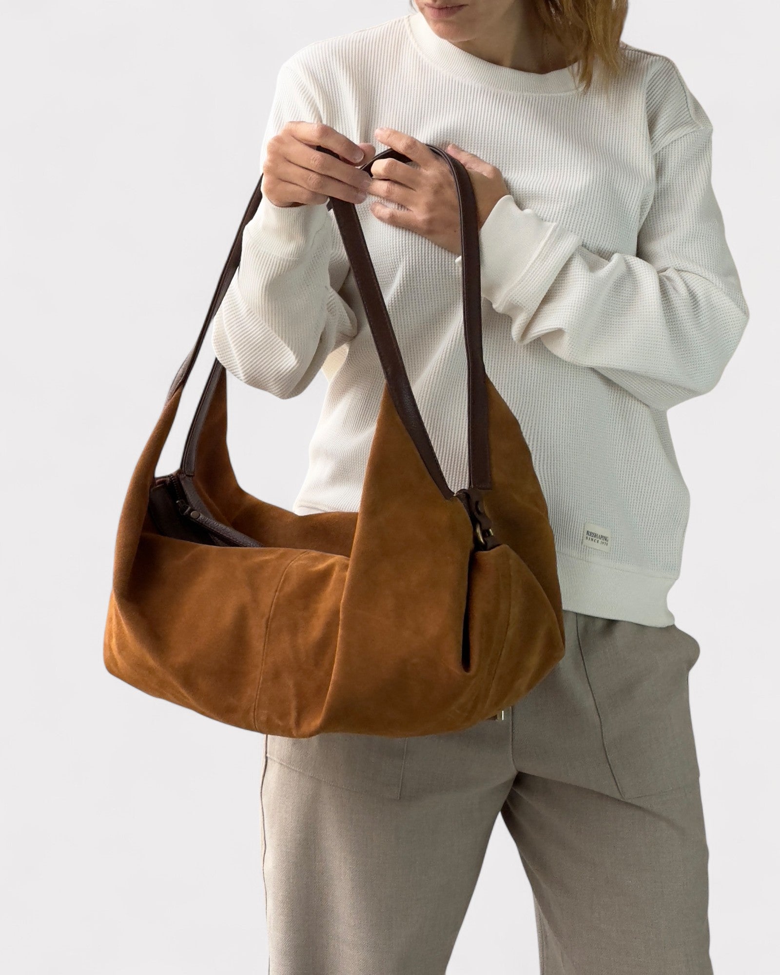 Person holding a tan leather bag against a white background