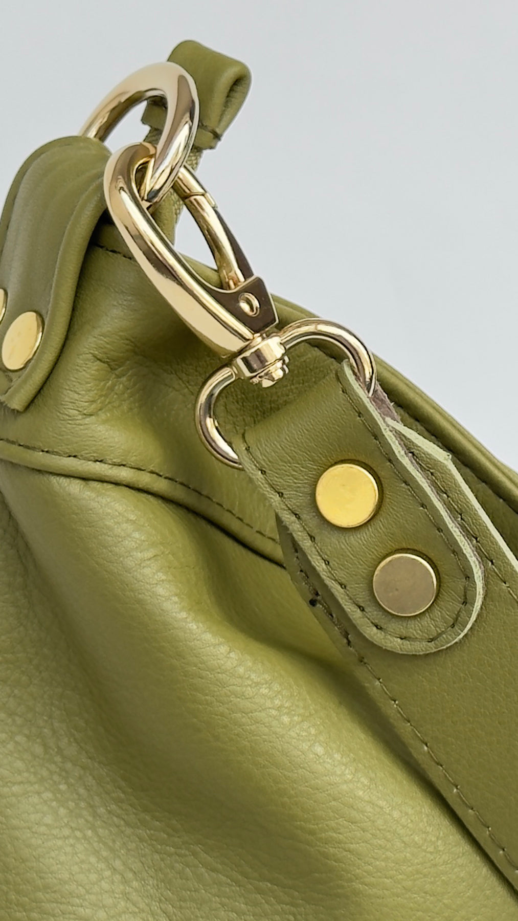 Close-up of a green leather handbag with gold hardware on a light gray background