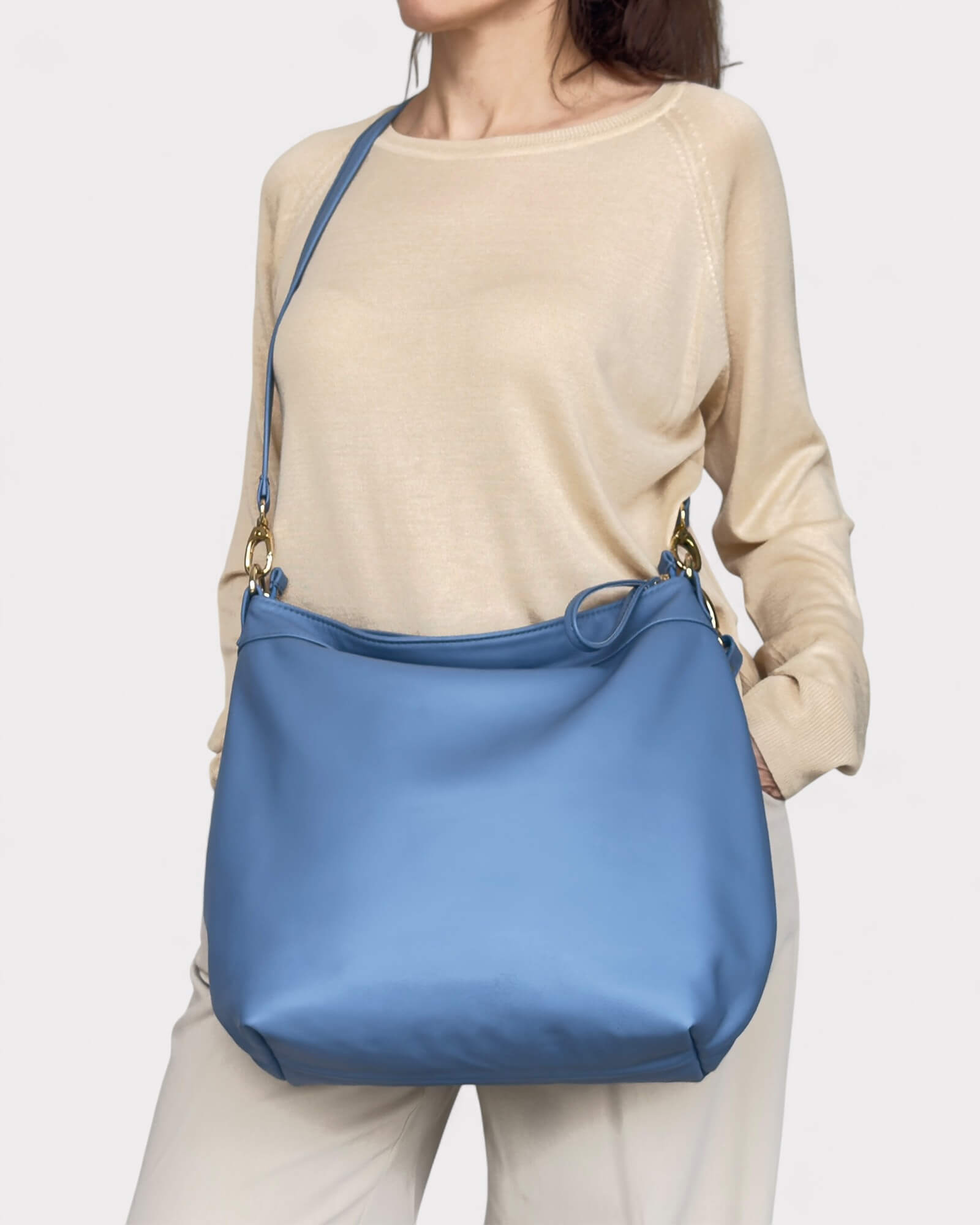 Person wearing a beige long-sleeve shirt and light-colored pants with a blue shoulder bag on a white background