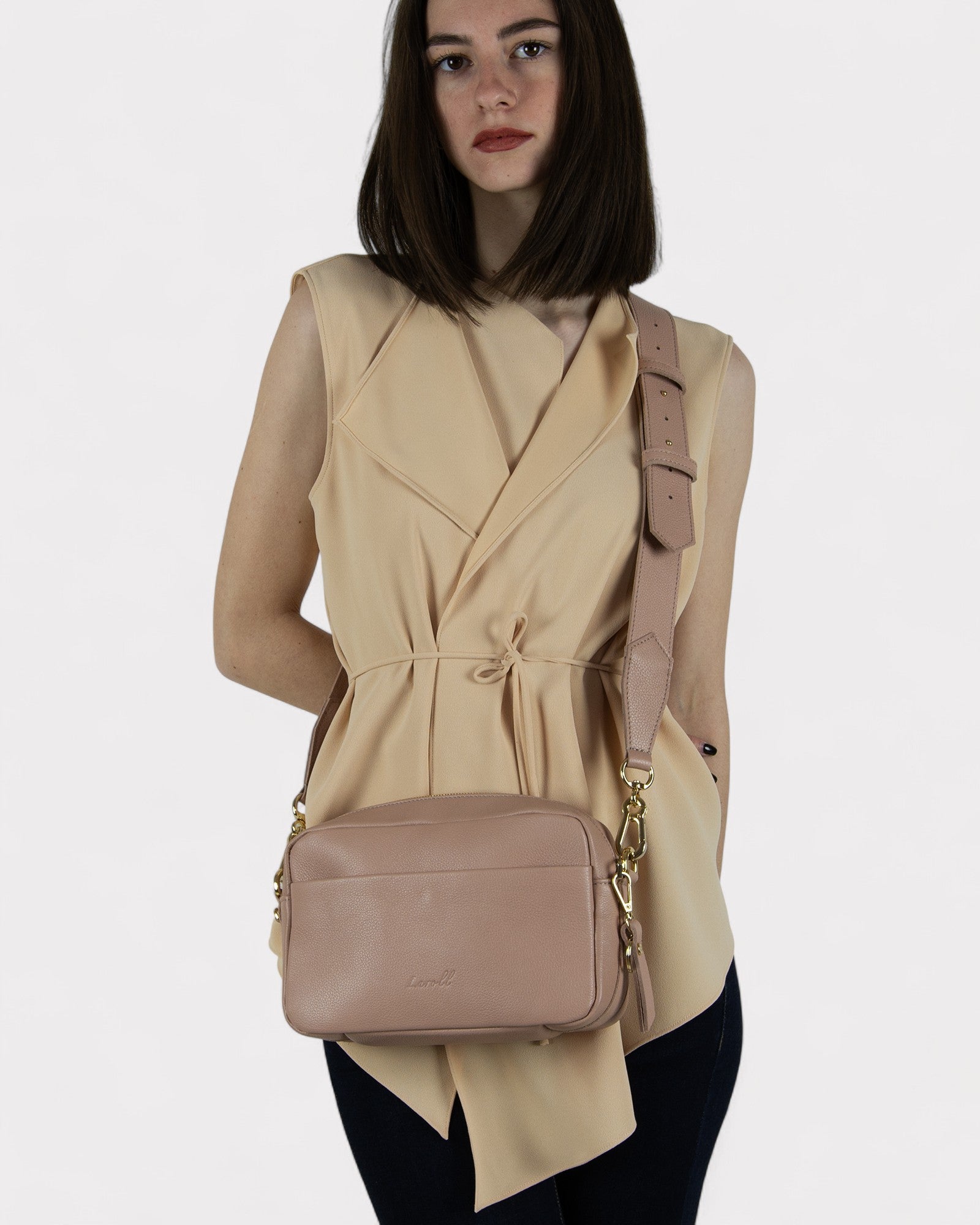 Woman wearing a dusty rose sleeveless top and carrying a matching dusty rose crossbody bag on a white background