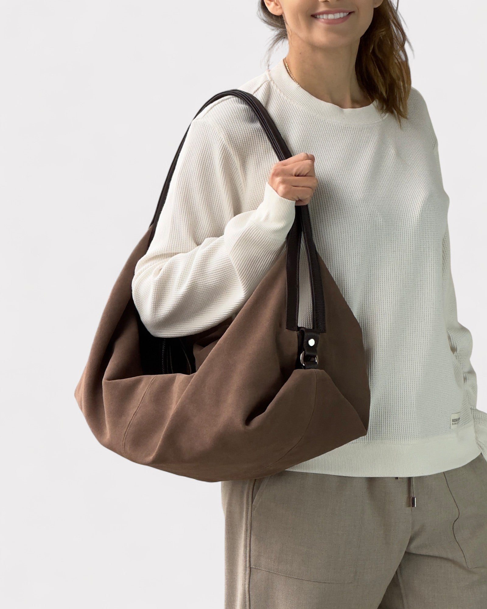 Person holding a taupe bag against a white background
