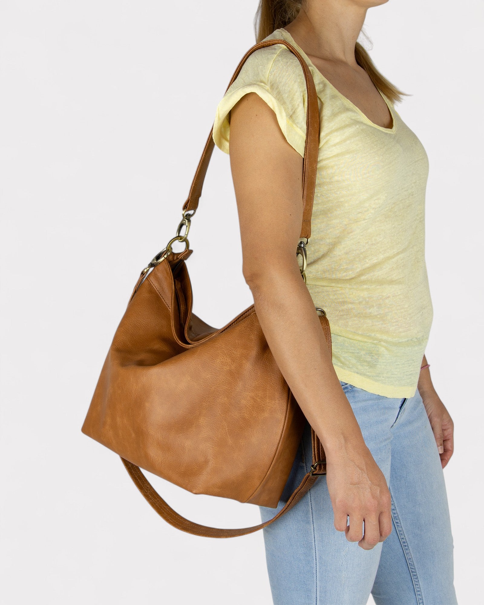 Woman holding a tan leather handbag against a plain background