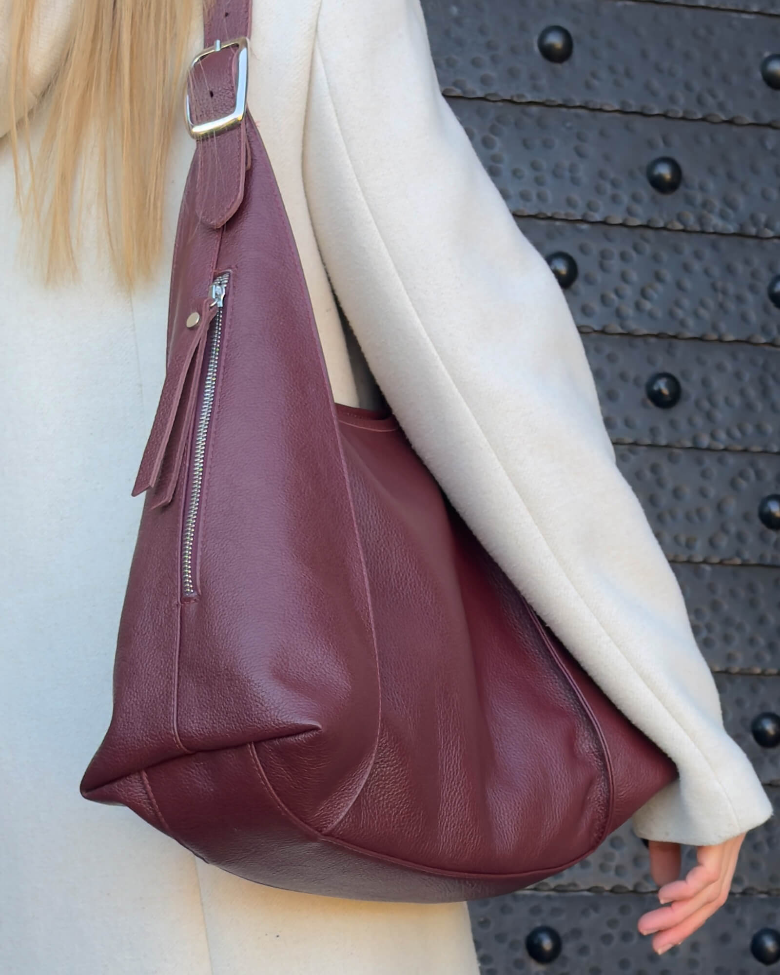 Burgundy leather handbag worn by a person against a textured black background
