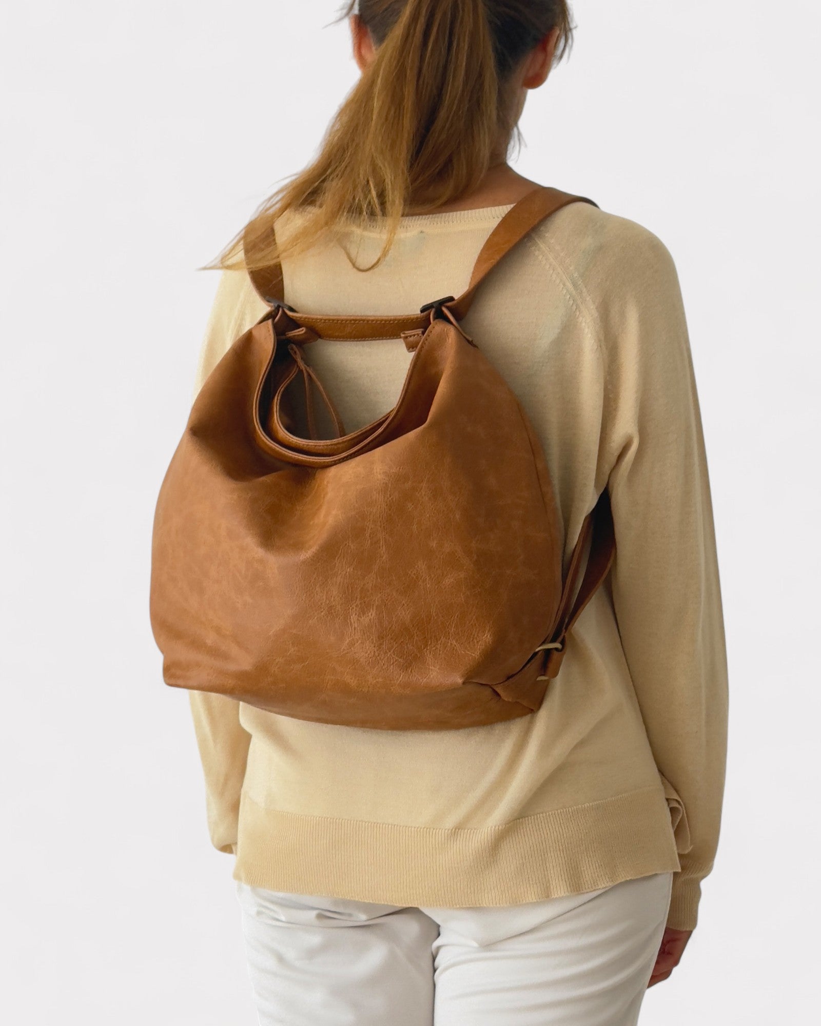 Person wearing a tan leather backpack on a plain background