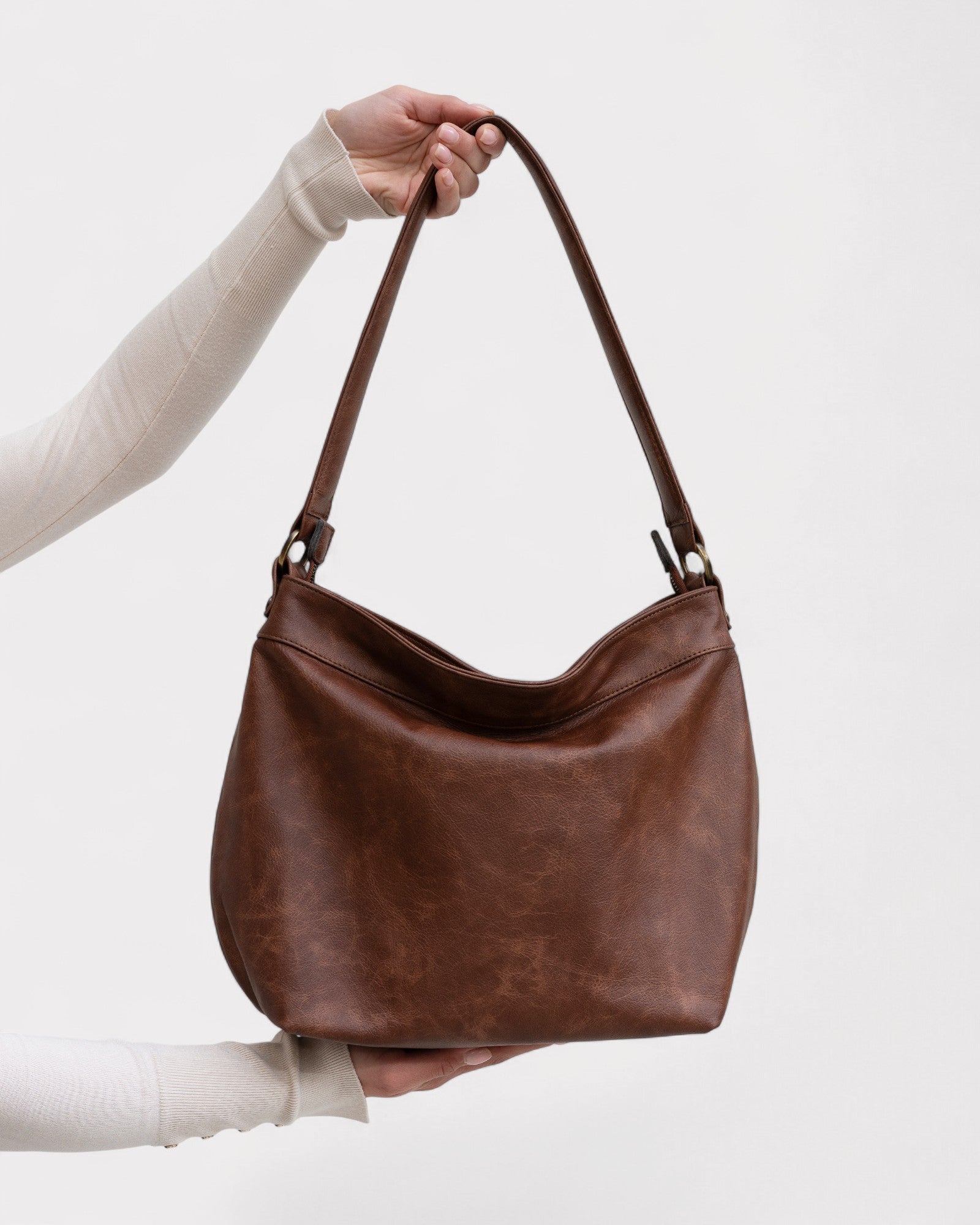 Brown leather handbag held by a person against a white background