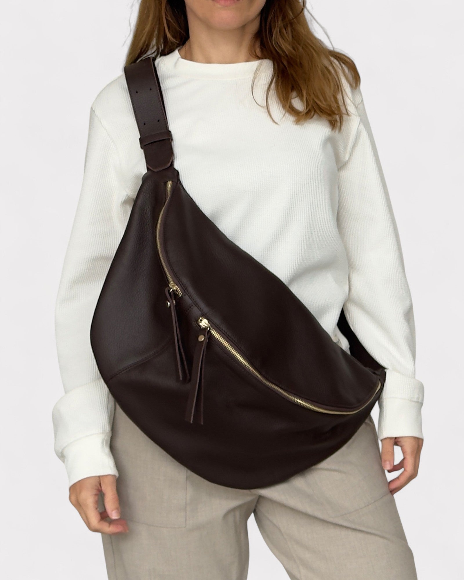 Person wearing a brown leather bag over one shoulder on a plain background