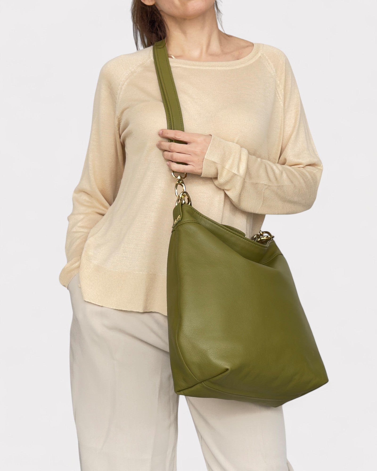 Person wearing a beige sweater and white pants with an olive green handbag on a light gray background