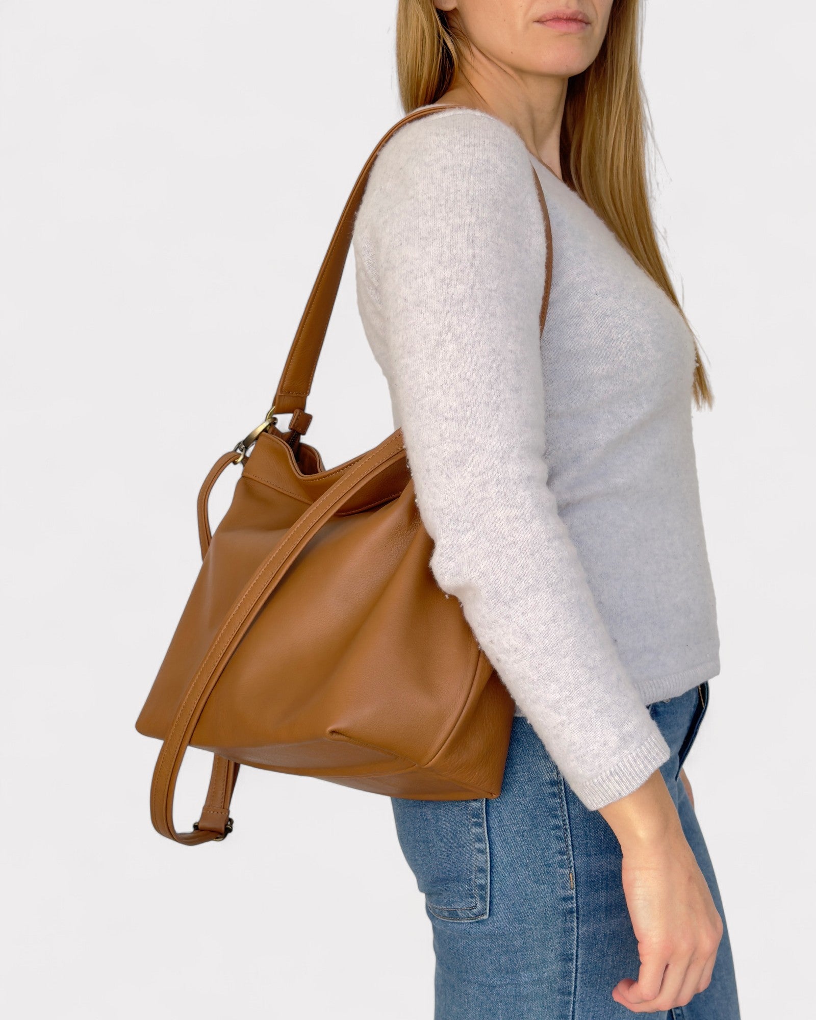 Woman carrying a tan leather handbag on a plain background