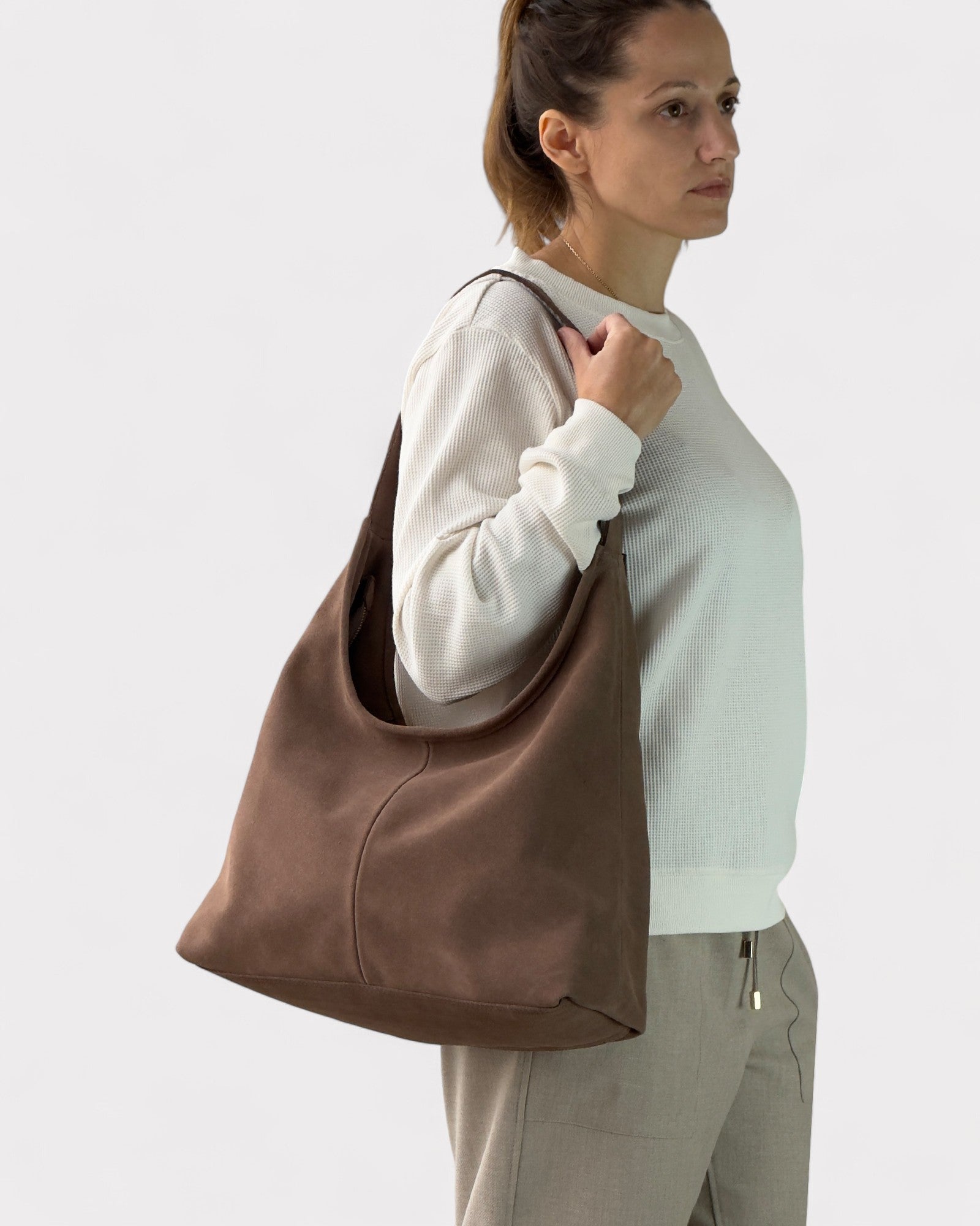 Woman holding a taupe leather bag against a plain background