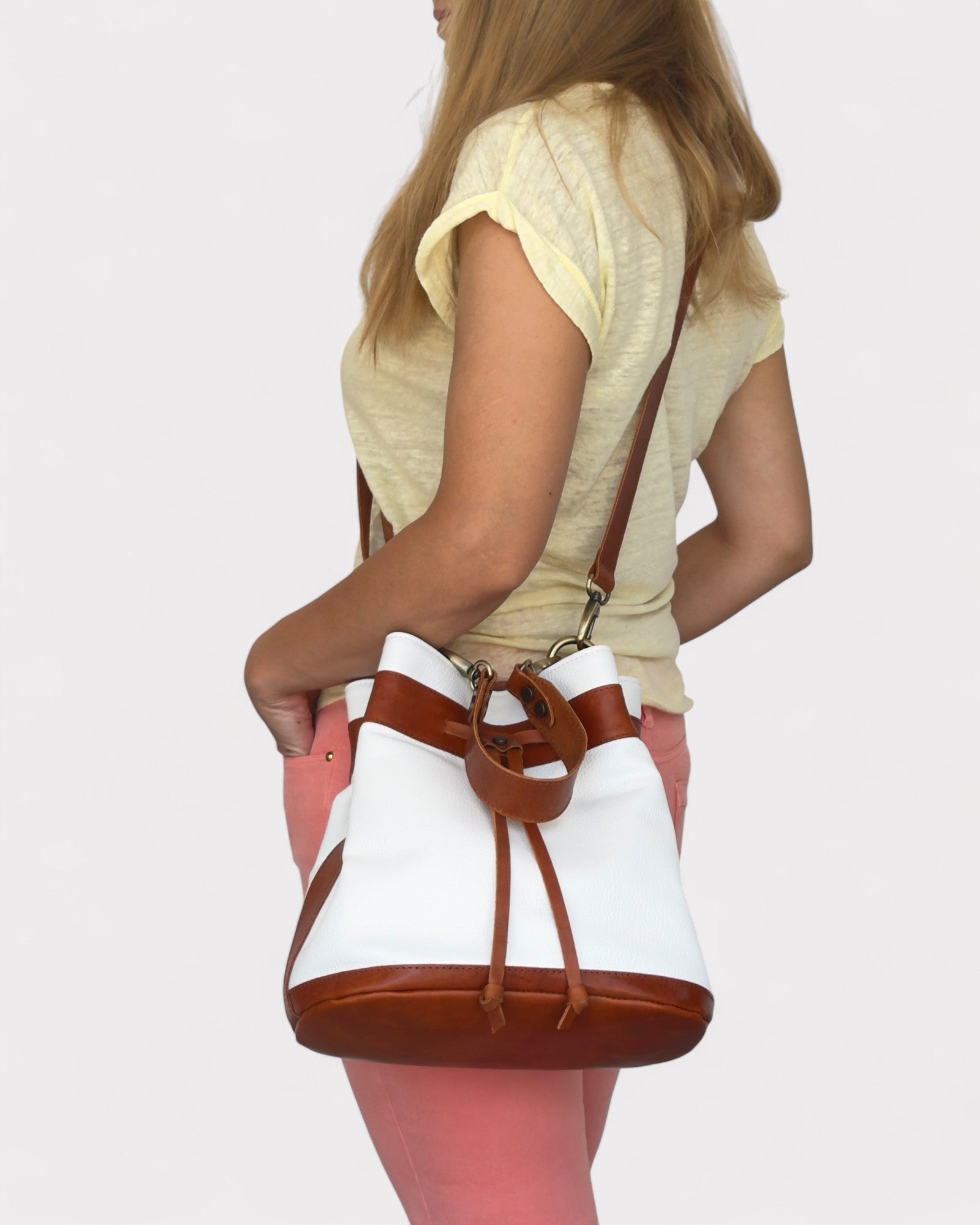 Person holding a white and brown bucket bag against a plain background