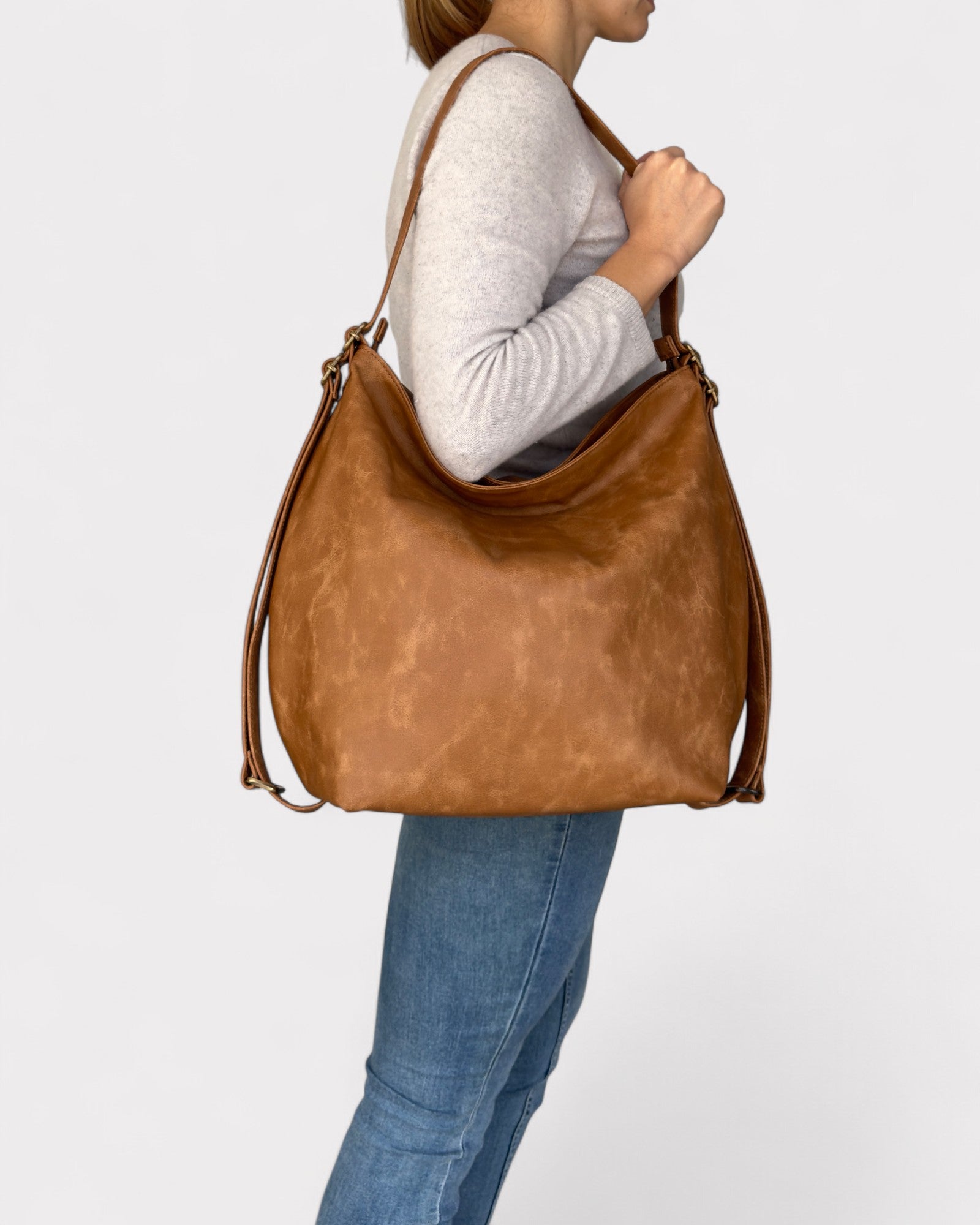 Person carrying a tan leather handbag on a light gray background