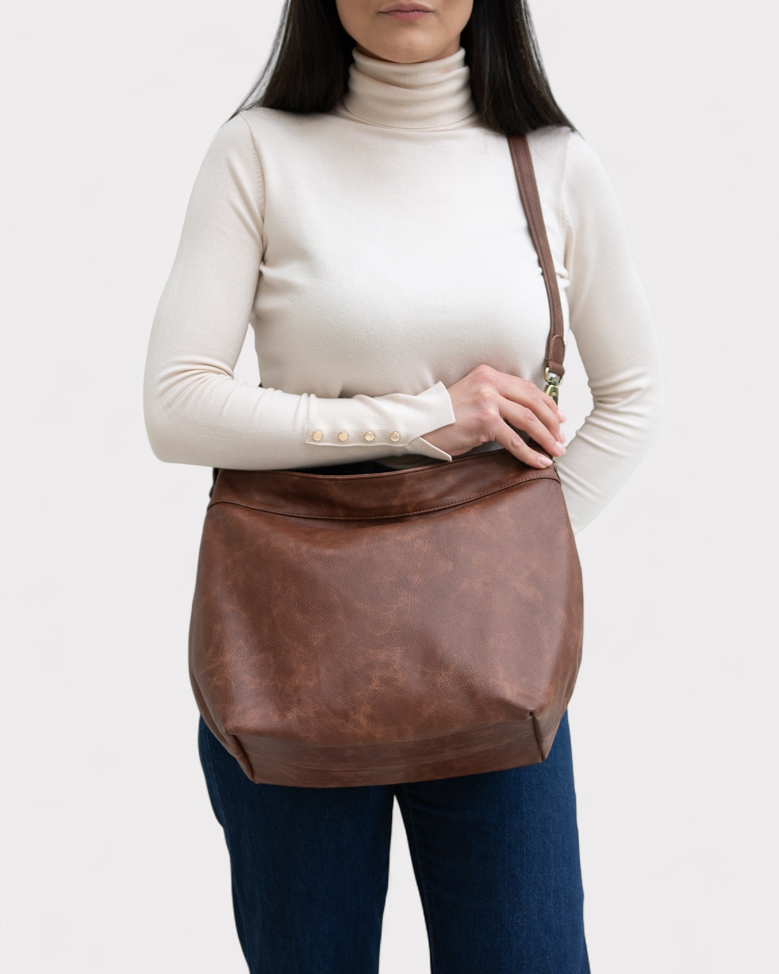 Person wearing a brown leather shoulder bag on a white background
