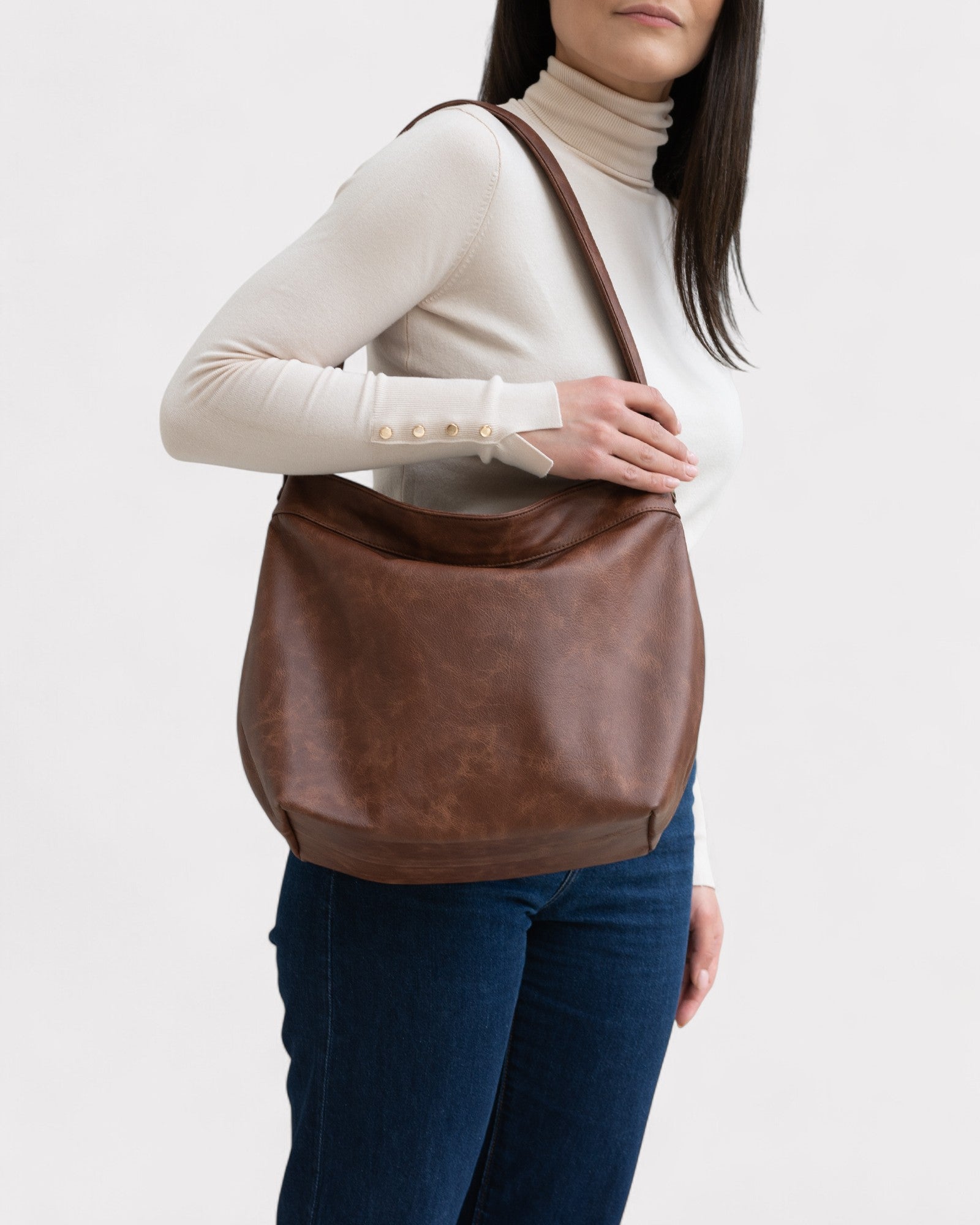 Person holding a brown leather bag against a white background