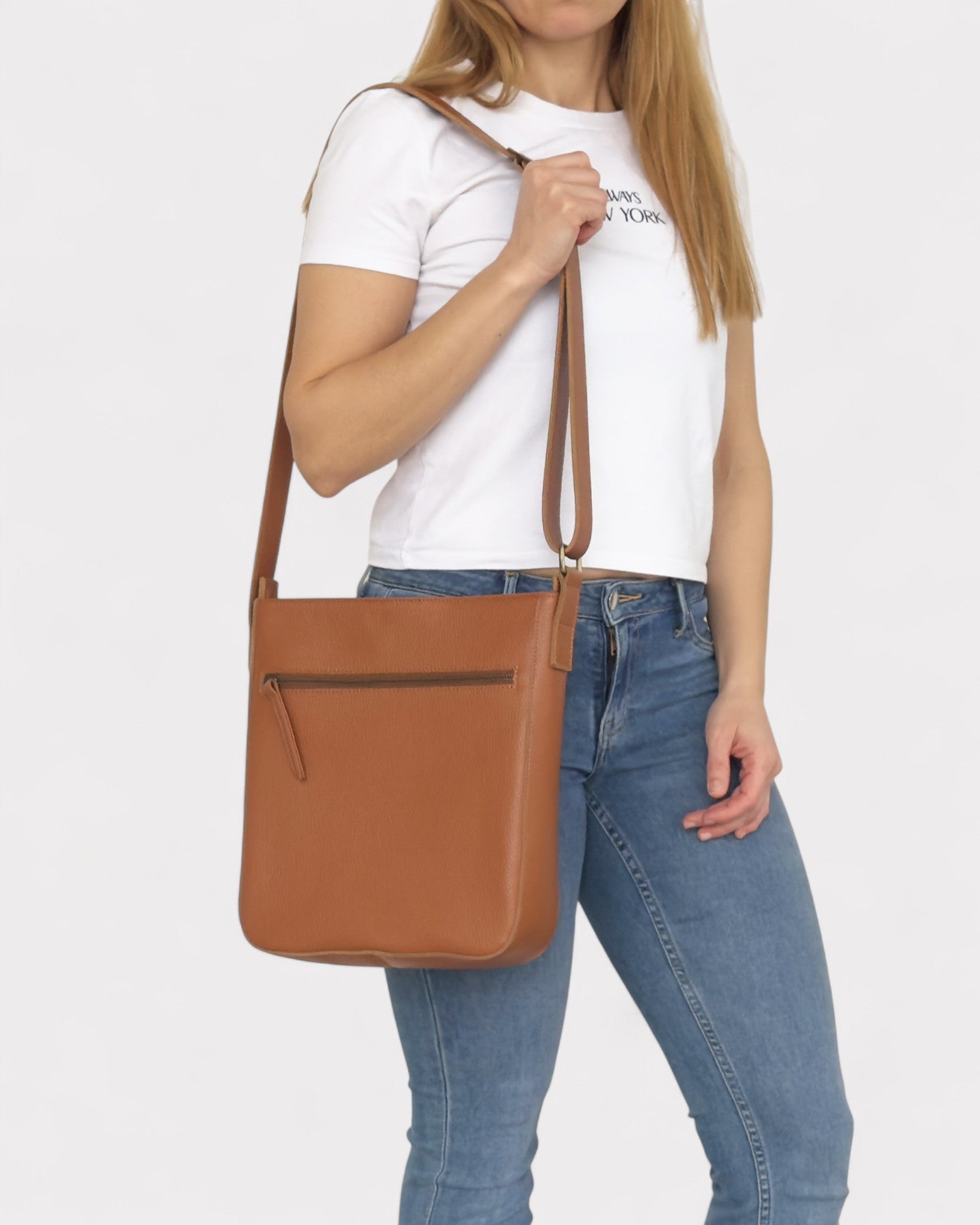 Person holding a tan leather crossbody bag against a white background
