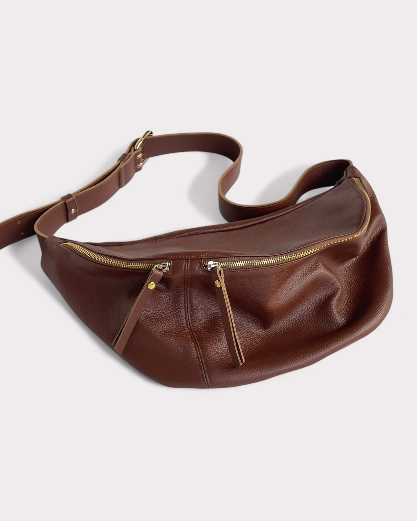 Brown leather fanny pack with gold zipper on a white background
