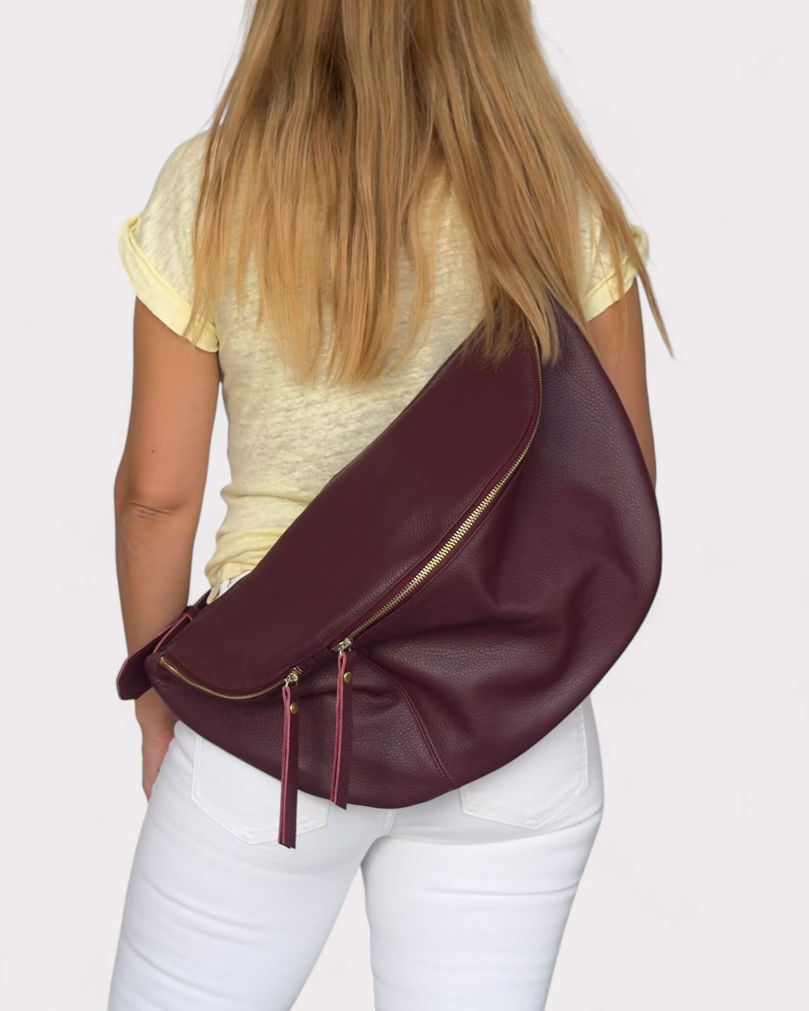 Person wearing a burgundy sling bag on a plain background