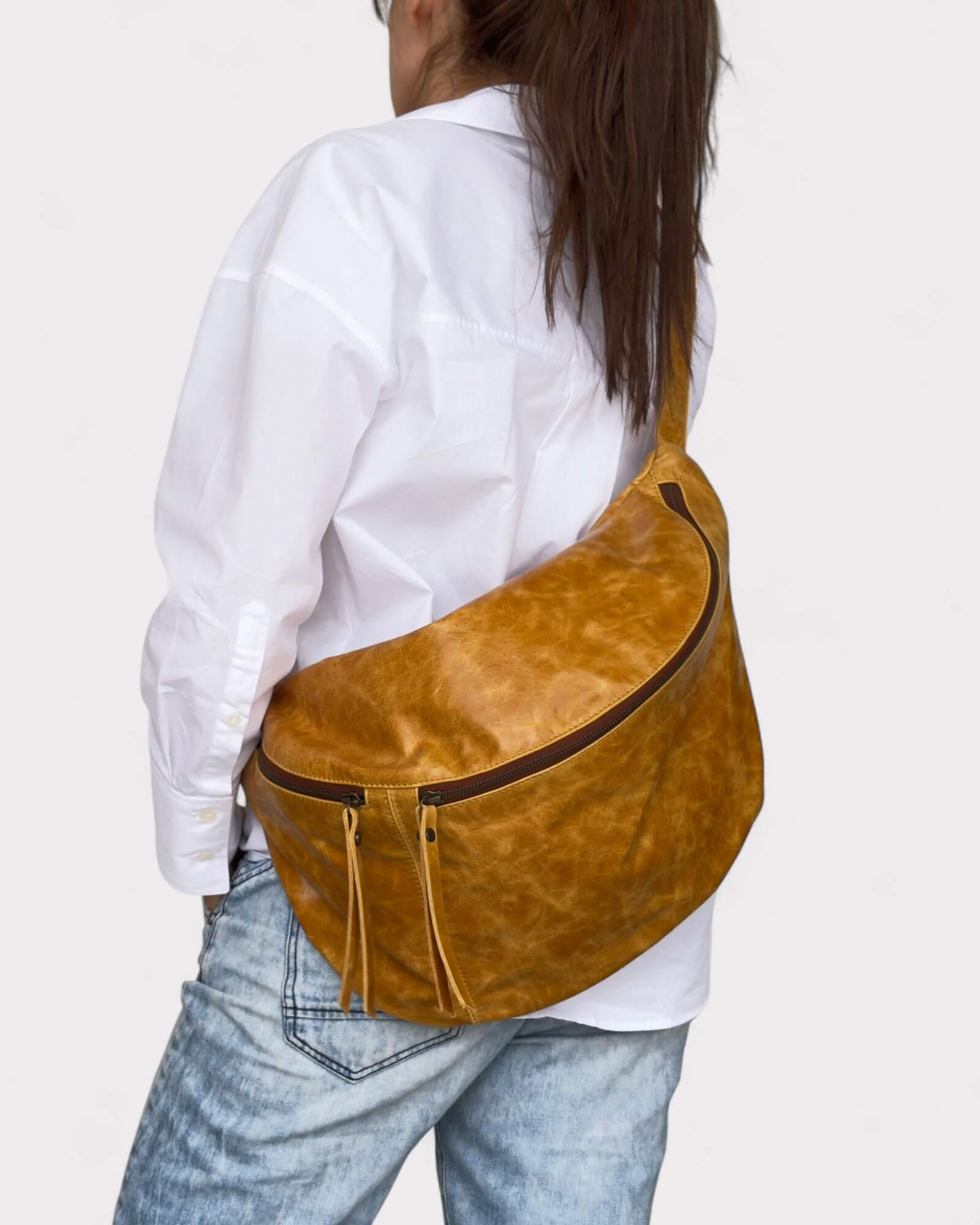 Person wearing a tan leather bag over one shoulder on a plain background