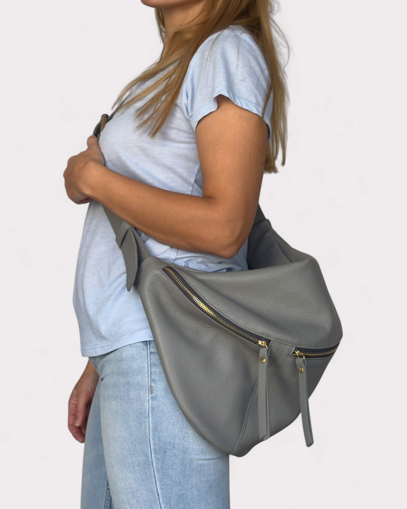 Person holding a gray shoulder bag against a plain background