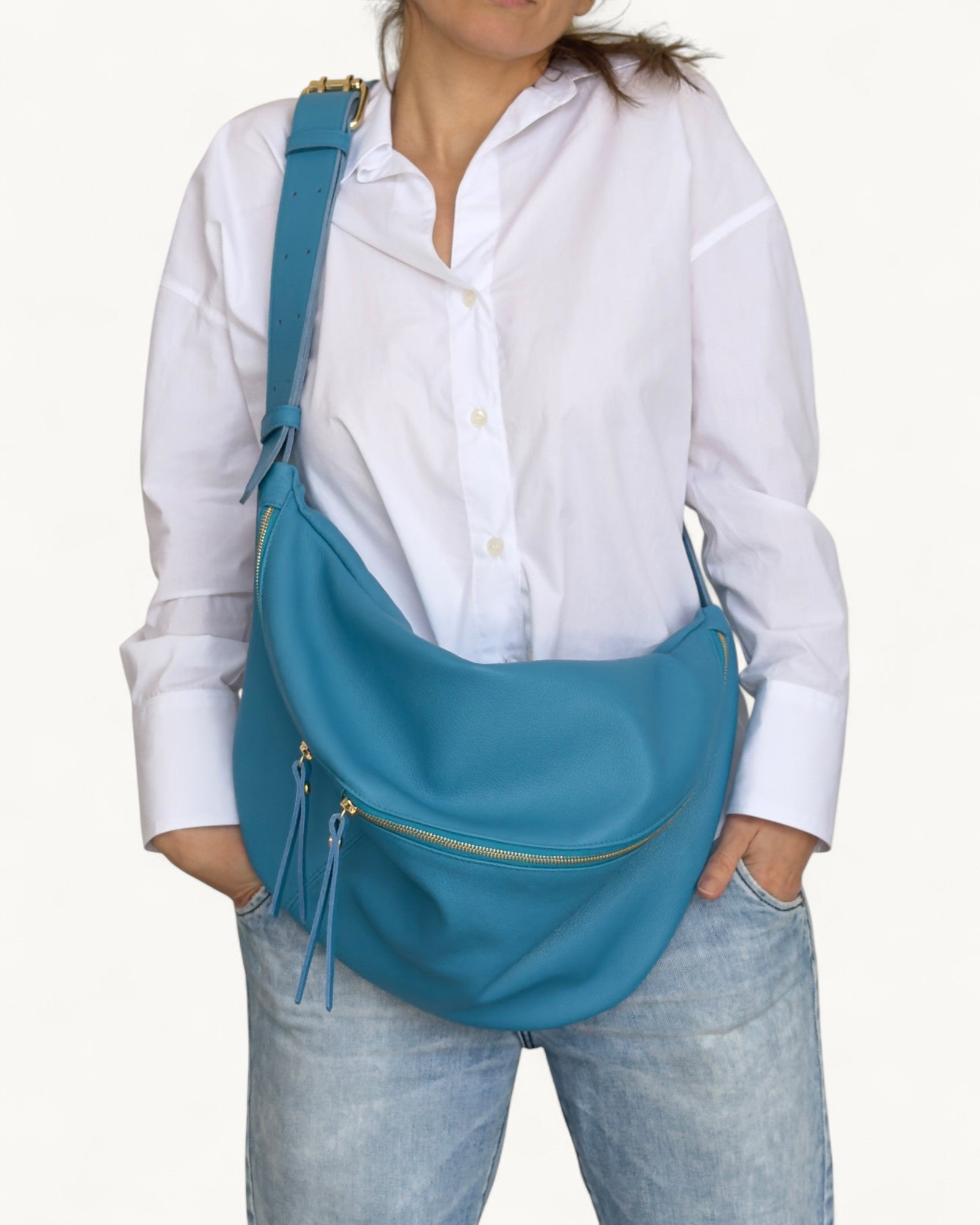 Person wearing a blue shoulder bag with a white shirt and light blue jeans on a white background