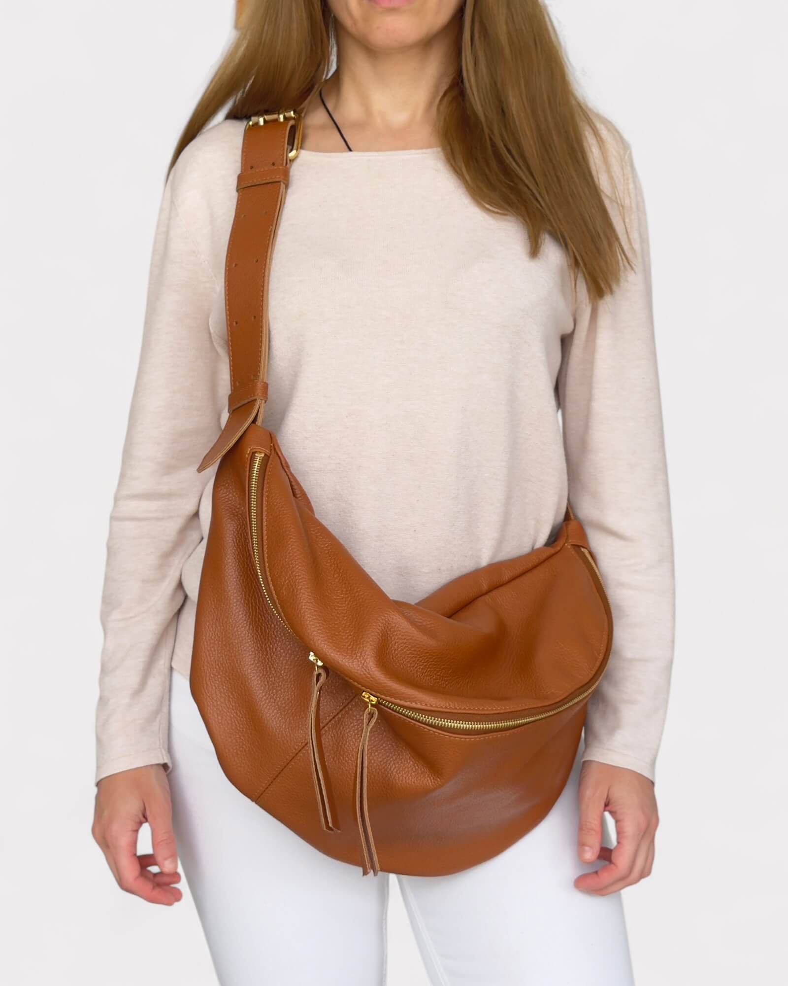Model wearing a tan leather sling bag on a plain background