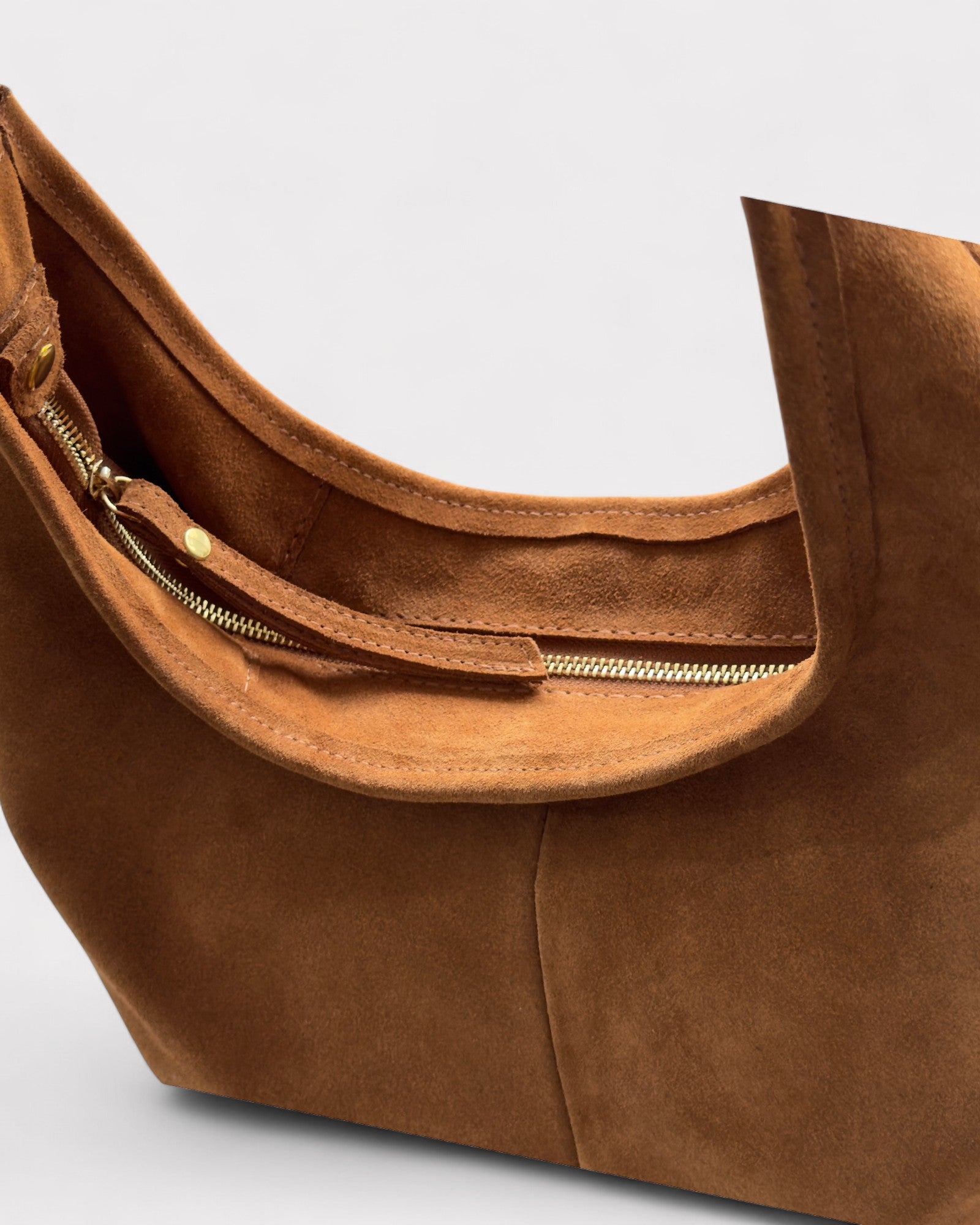 Tan suede handbag with gold zipper on a light gray background