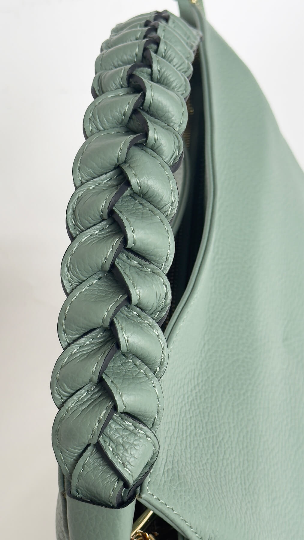 Close-up of a green handbag with braided detail on a light gray background