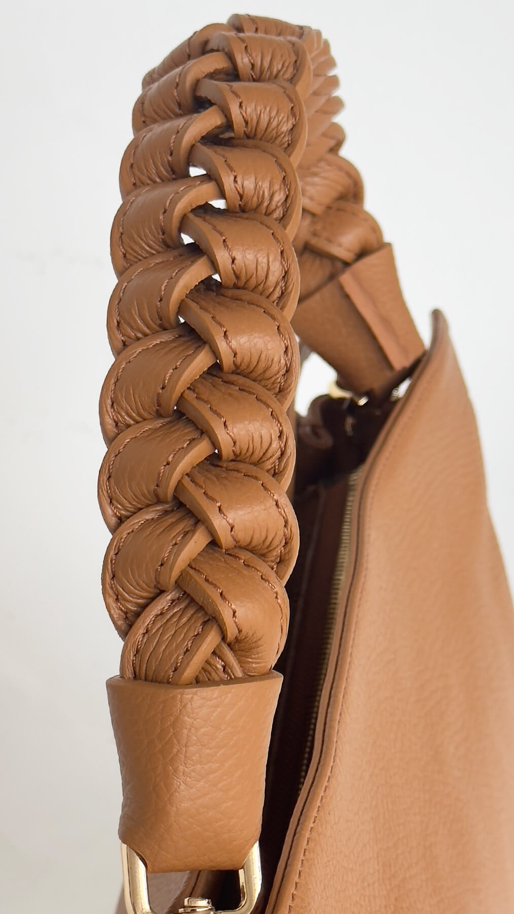 Close-up of a tan leather handbag with braided handle on a light gray background