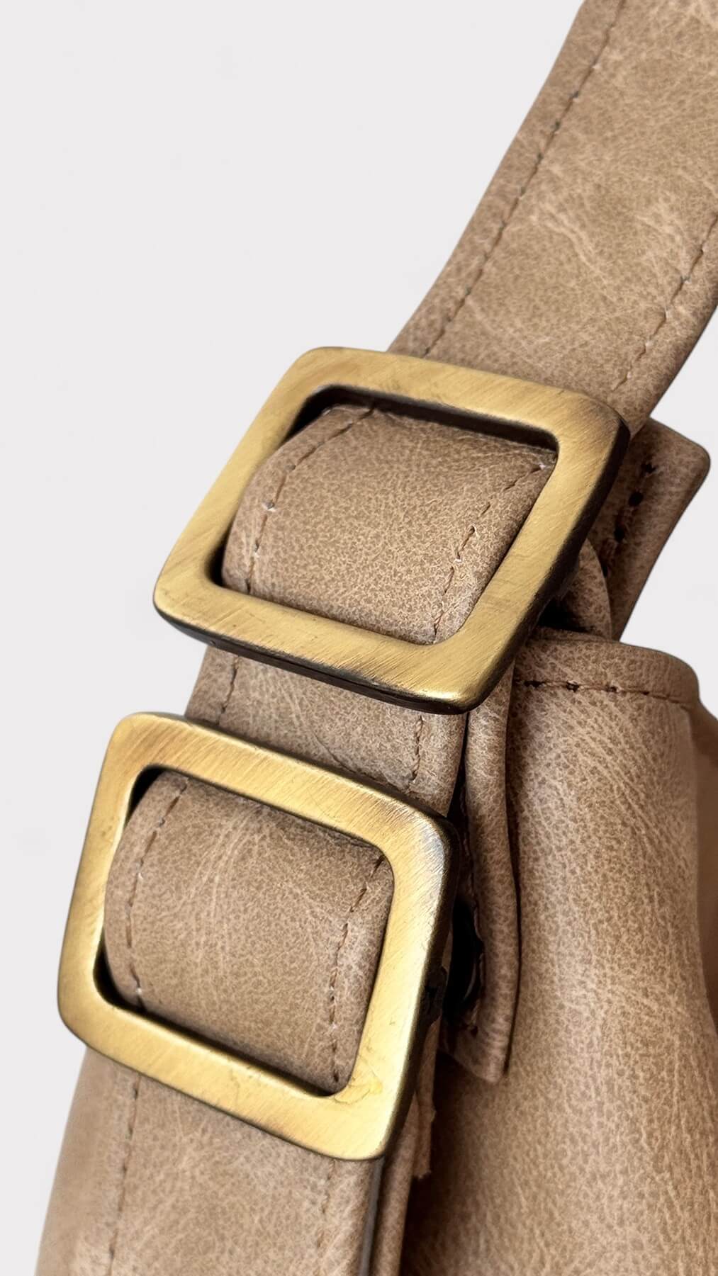 Beige leather bag with brass buckles on a light gray background