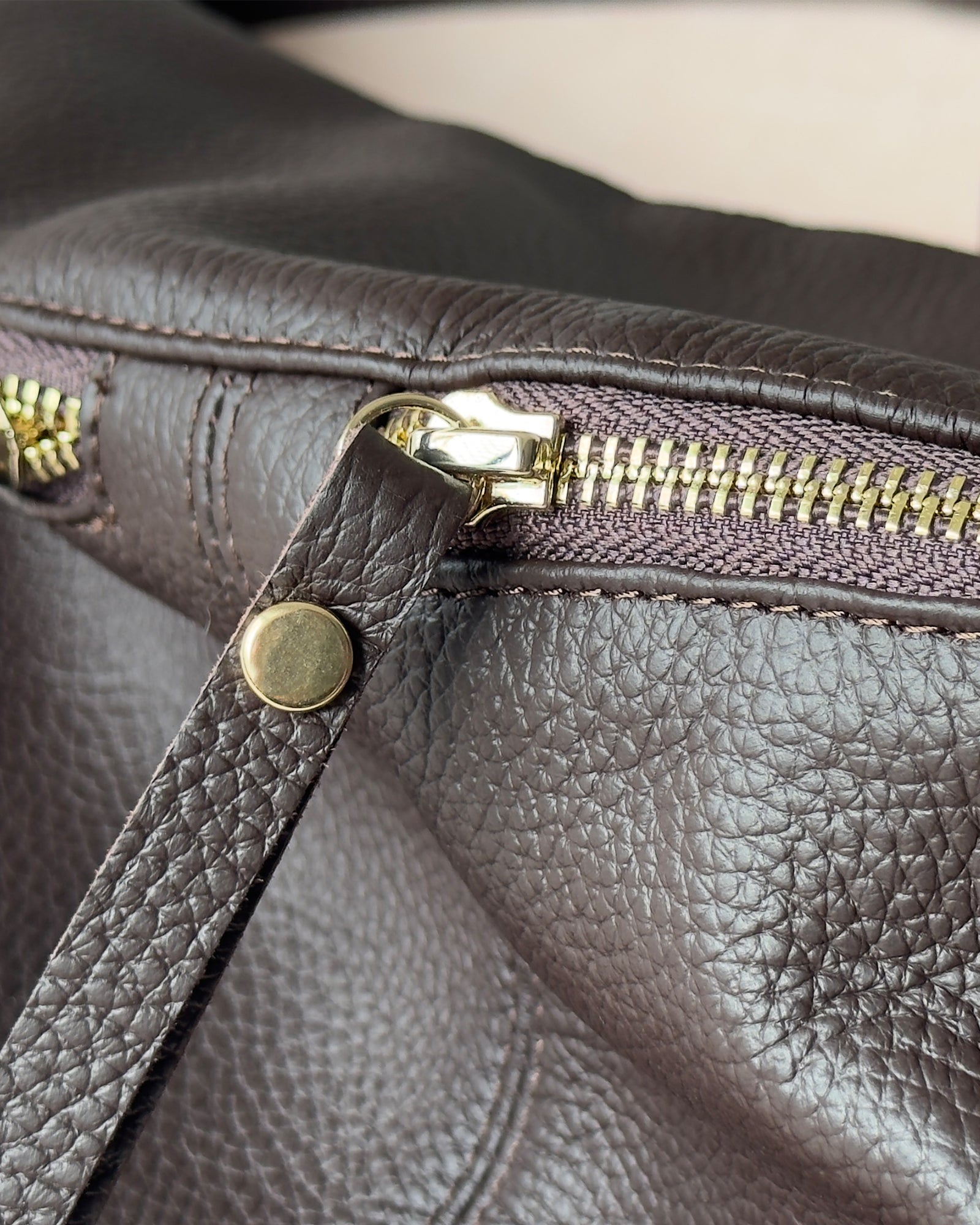 Close-up of a brown leather bag with gold zipper and hardware.