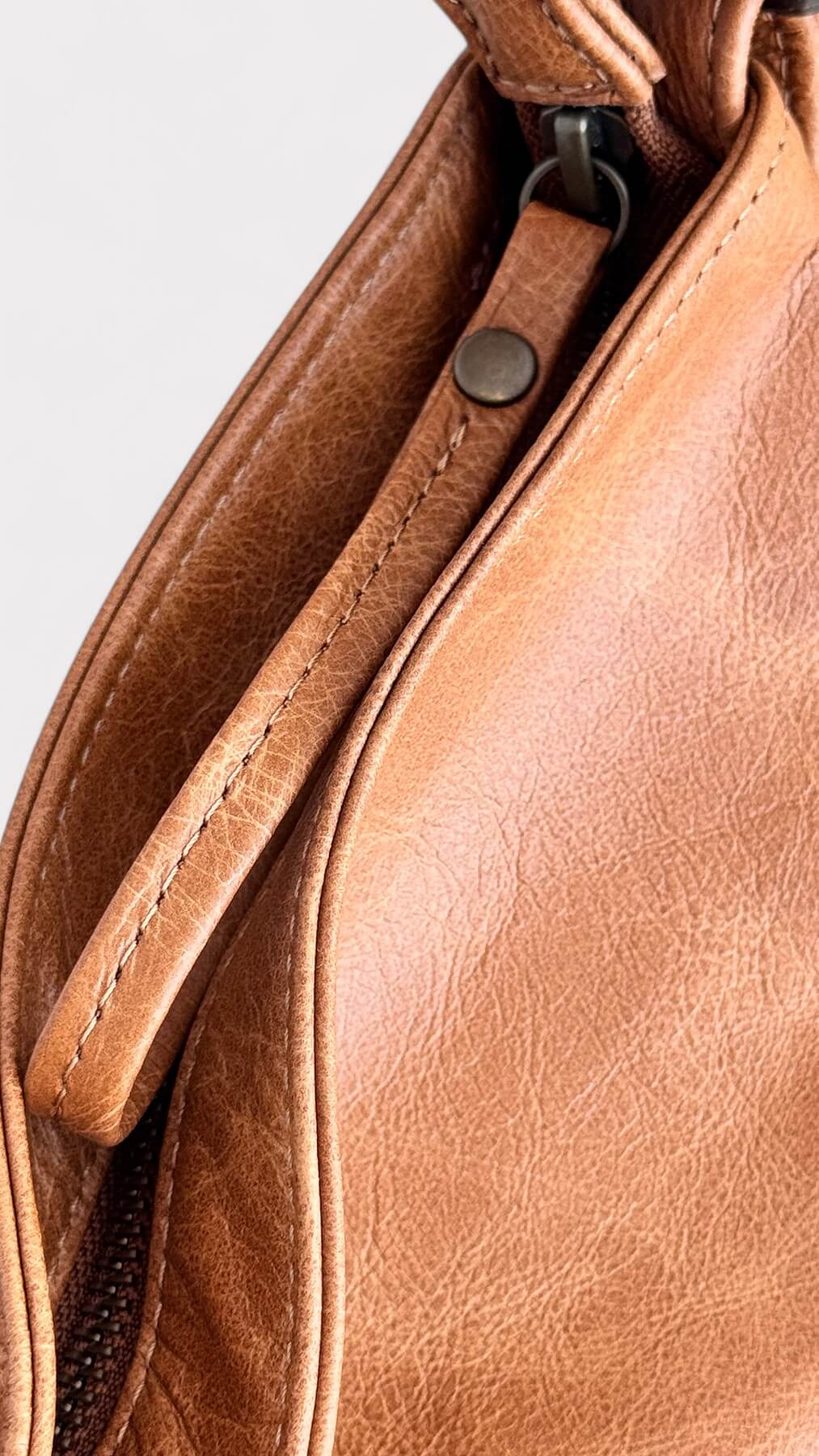 Close-up of a tan leather handbag with a strap on a light gray background