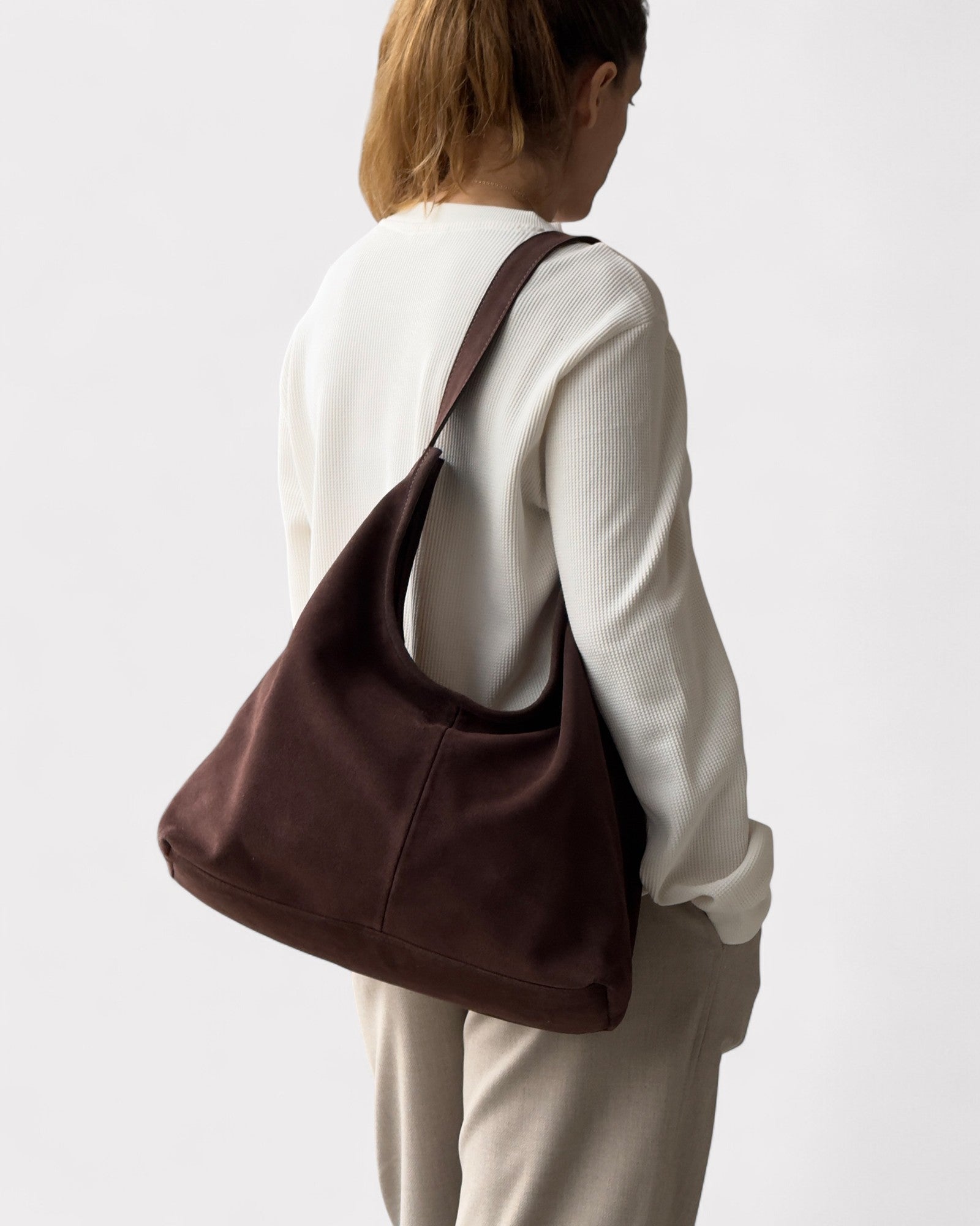 Person wearing a brown shoulder bag on a plain background