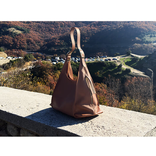 Tan leather handbag on a ledge with a scenic background of mountains and trees.