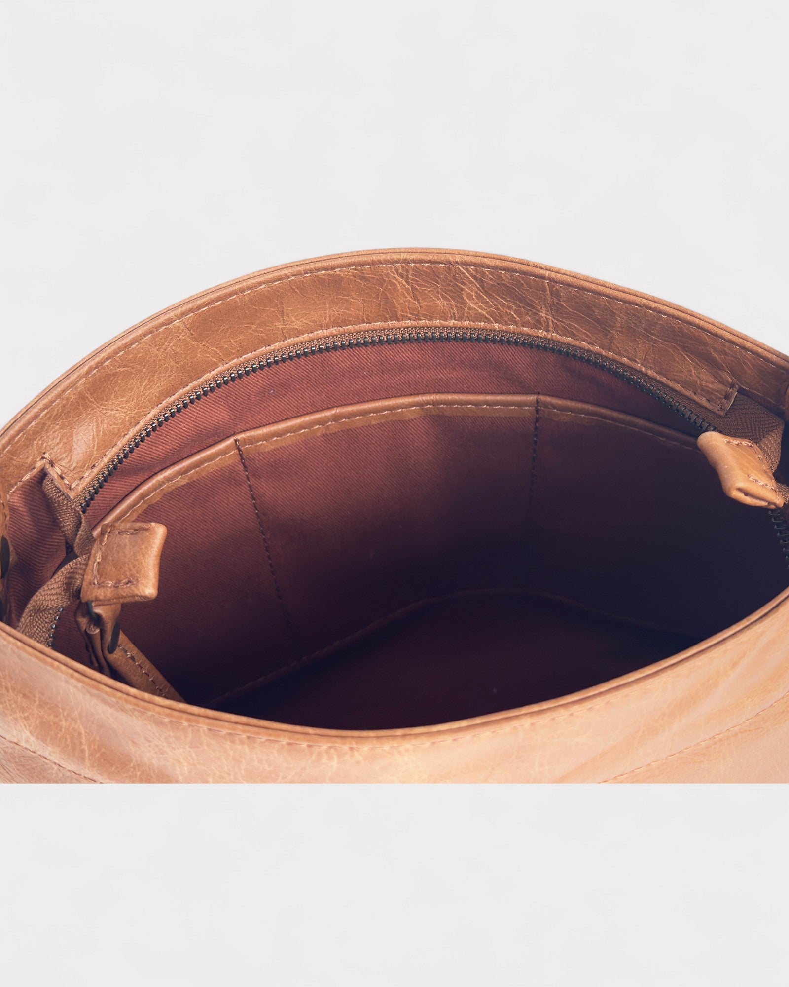 Close-up of a tan distressed  leather bag with a zipper on a light gray background