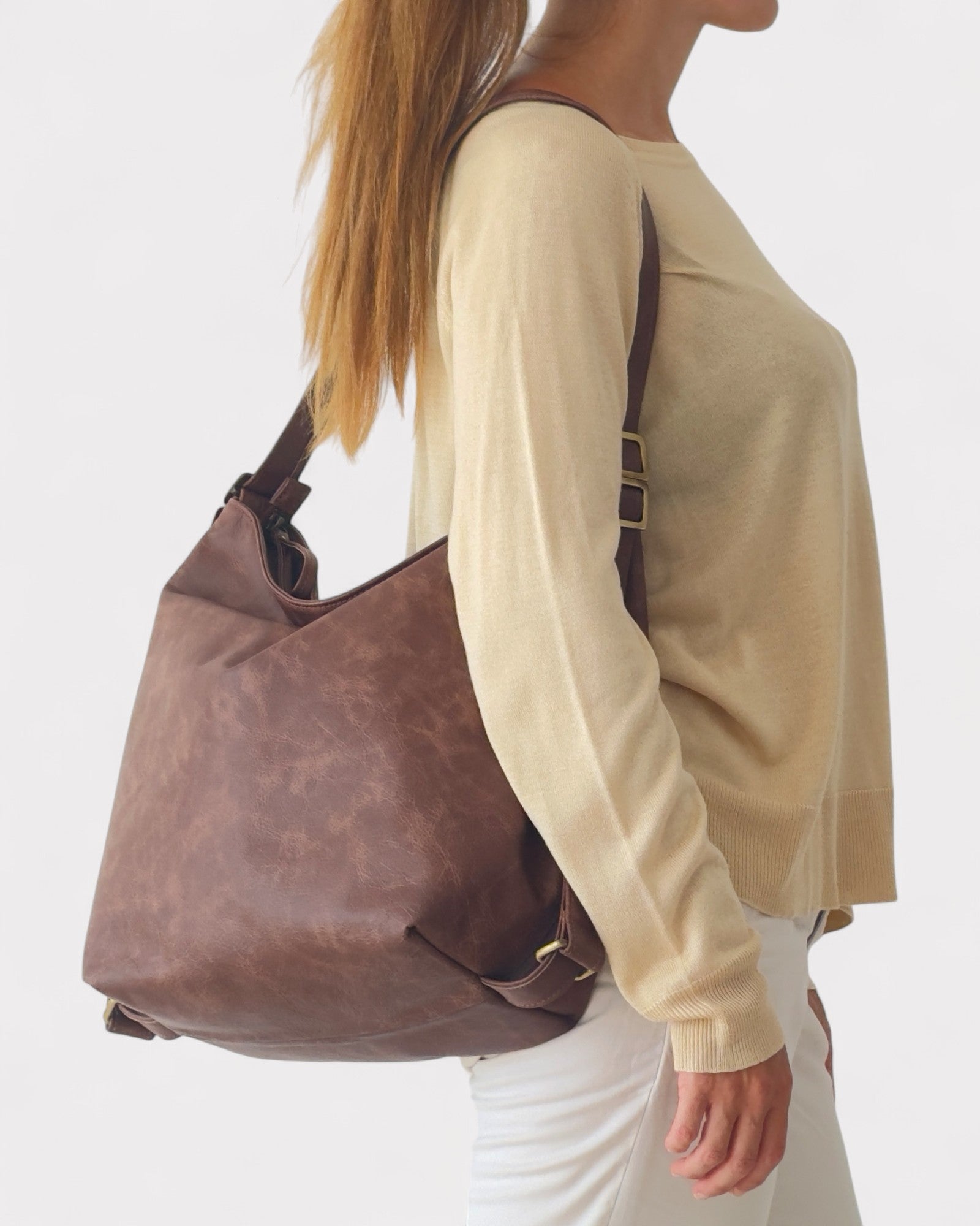 Person wearing a beige sweater and white pants with a brown leather handbag on a white background