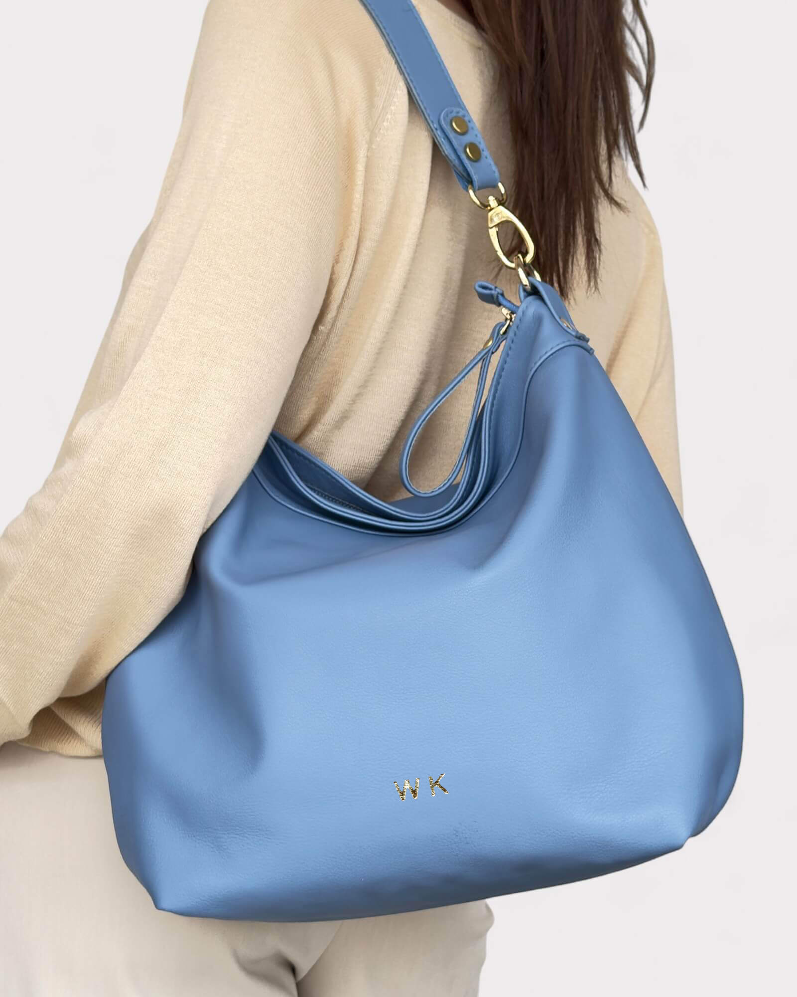 Blue handbag with gold hardware worn by a person on a light background with monogram