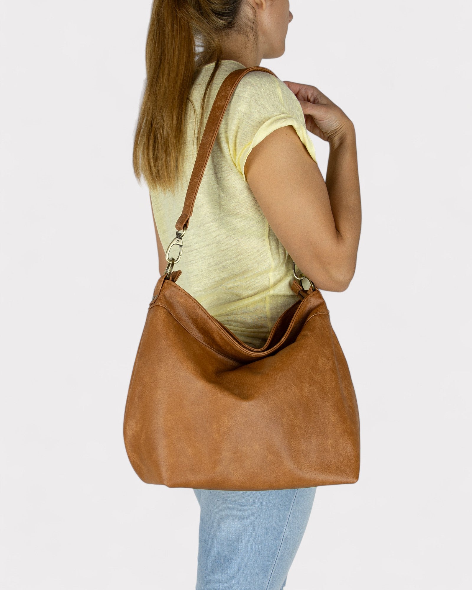 Woman carrying a Tan distressed leather handbag on a plain background