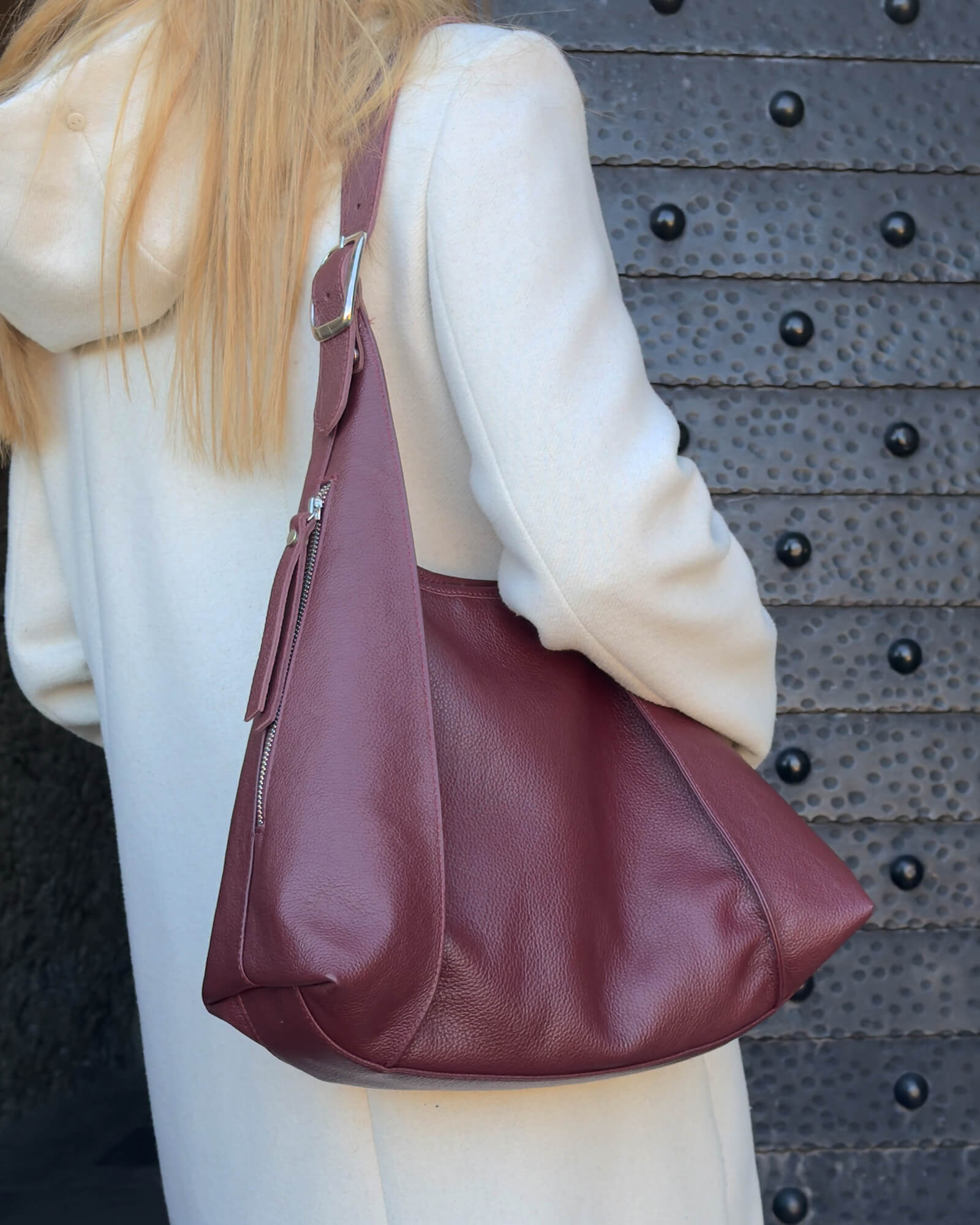 Person wearing a beige coat with a maroon handbag against a textured dark background