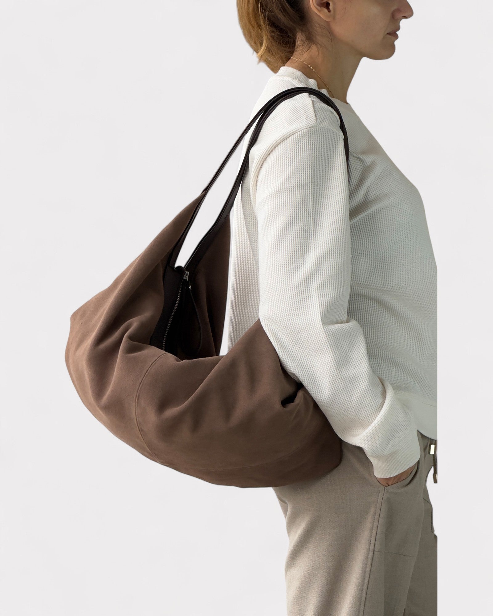 Person wearing a taupe shoulder bag on a plain background