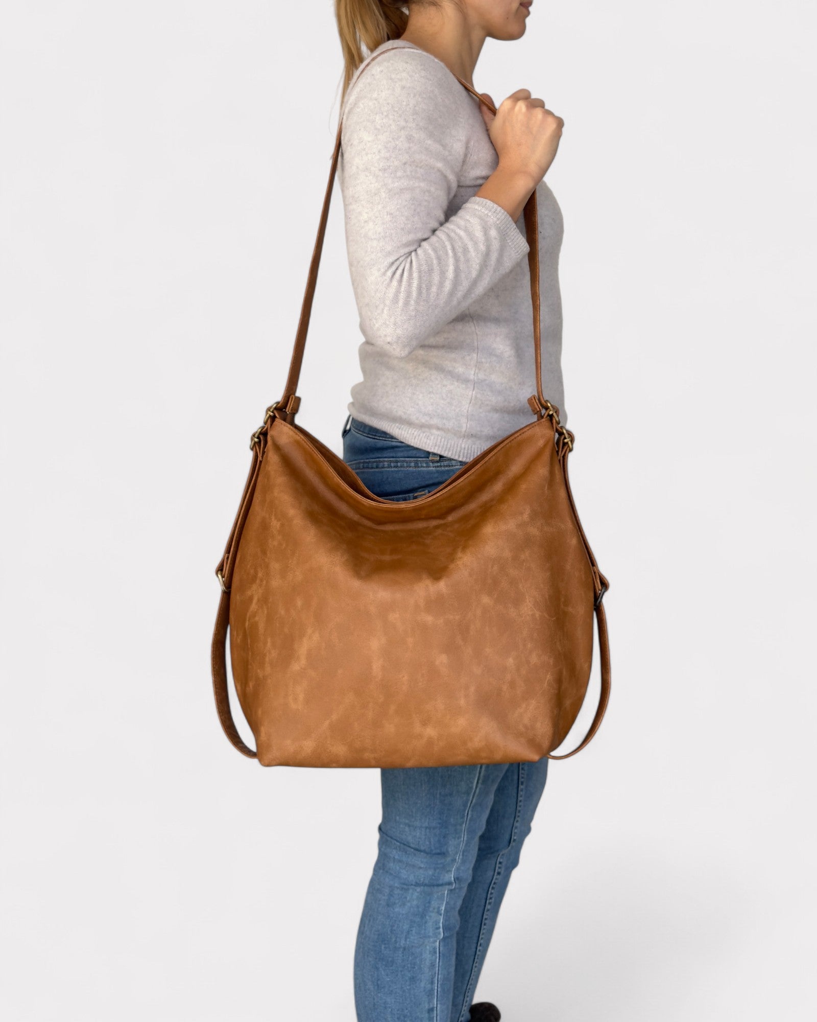 Person holding a tan leather handbag against a white background